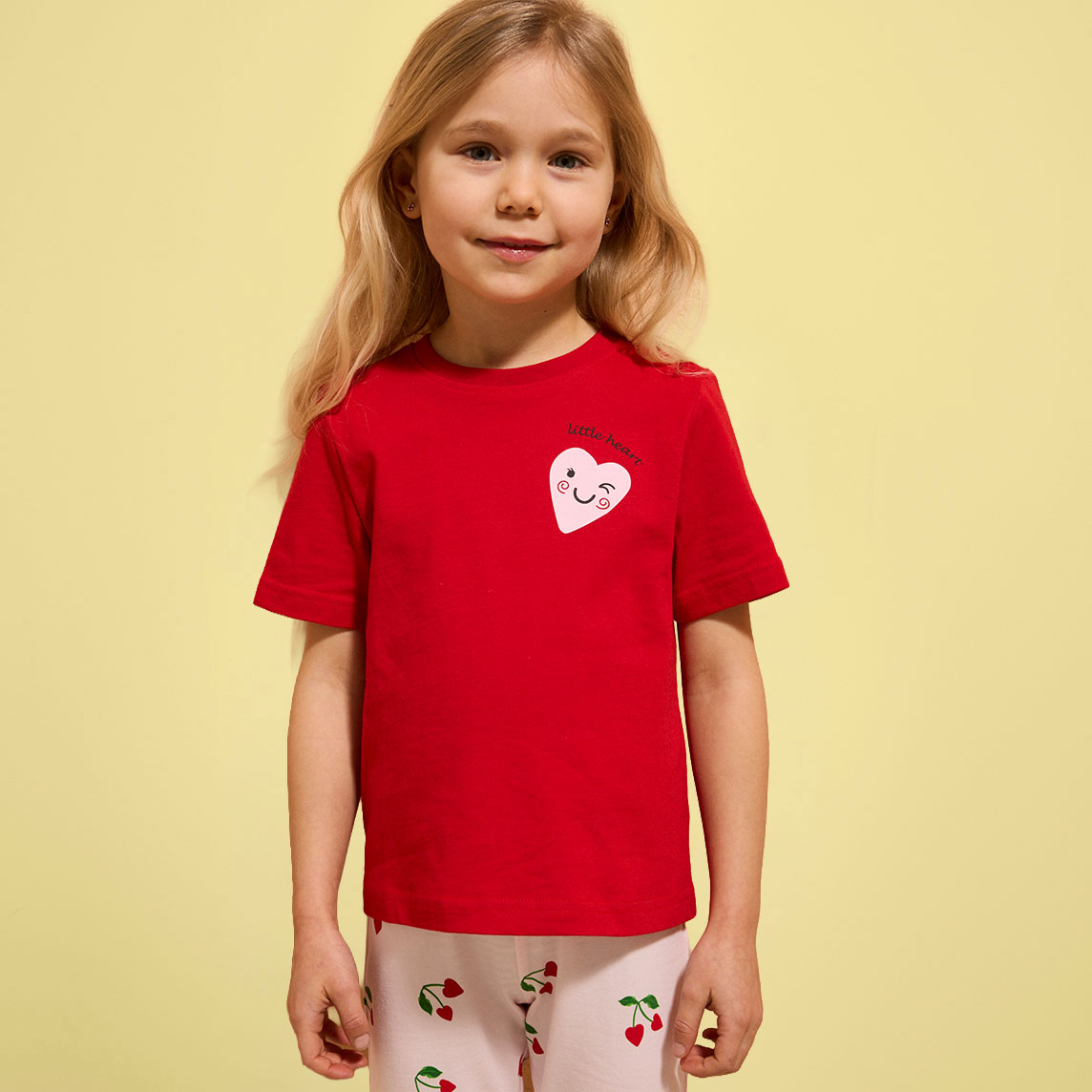 Ein kleines Mädchen trägt ein rotes T-Shirt mit rosa Herzmotiv.