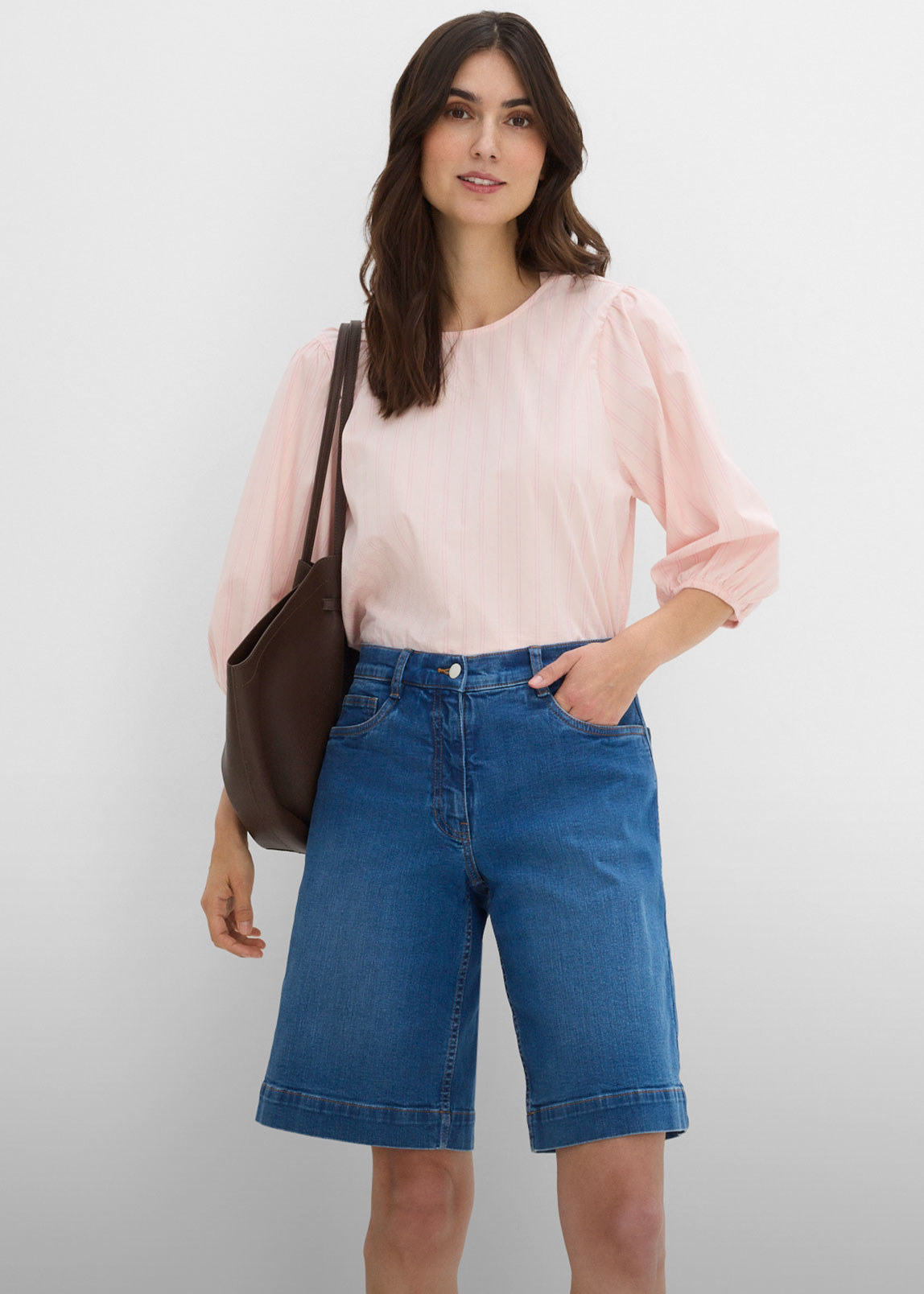 Zartrosa Bluse mit 3/4-Ärmeln, blaue Jeans-Bermudas und eine braune Schultertasche.