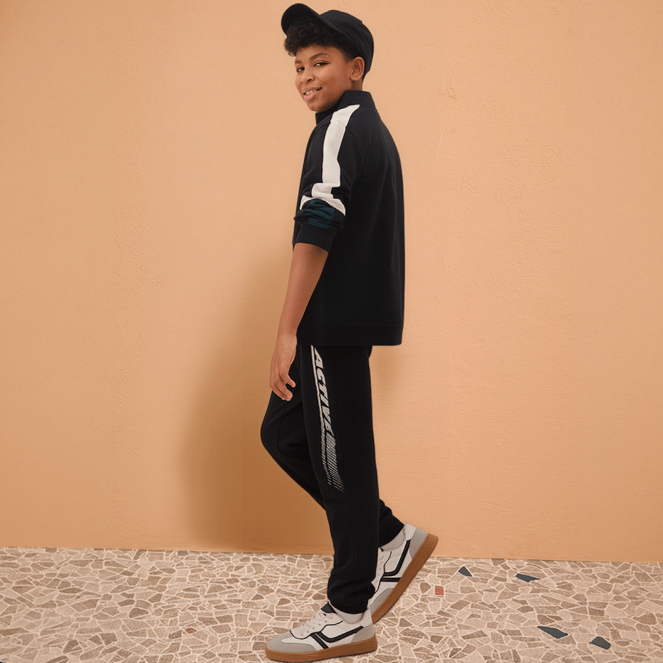 Sportliches Outfit mit schwarzem Trainingsanzug, weißen Streifen und passenden Sneakern. Bequem und stylish.