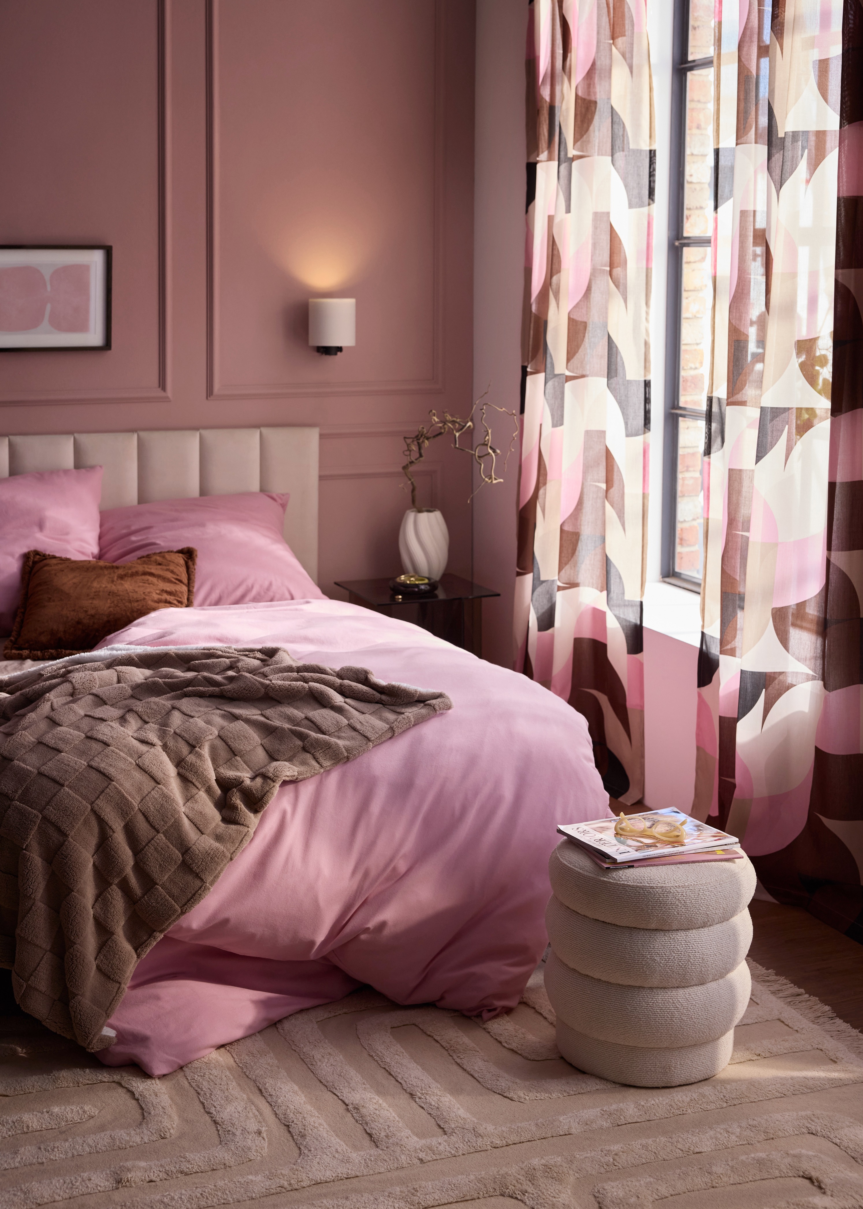 Pinke Bettwäsche, eine braune Decke, gemusterte Vorhänge und ein flauschiger Teppich.