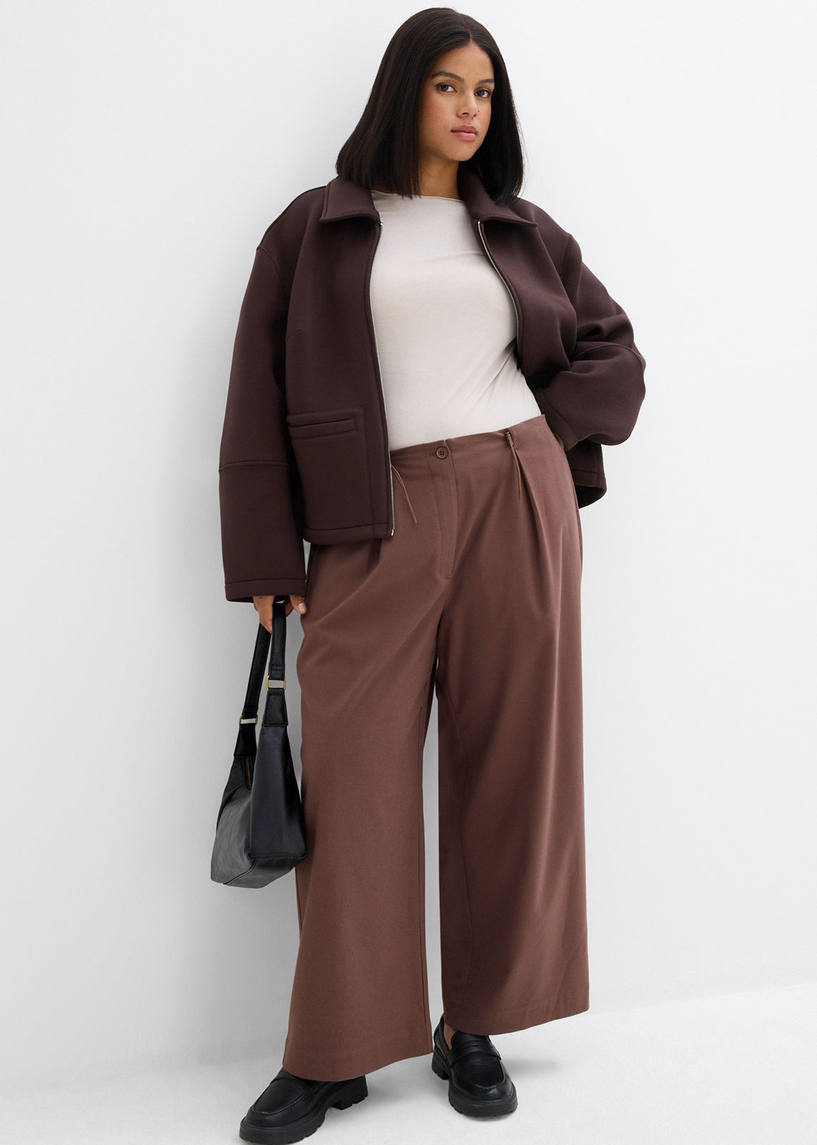 Braune Jacke, weißes Top und weite Hose in Erdtönen.