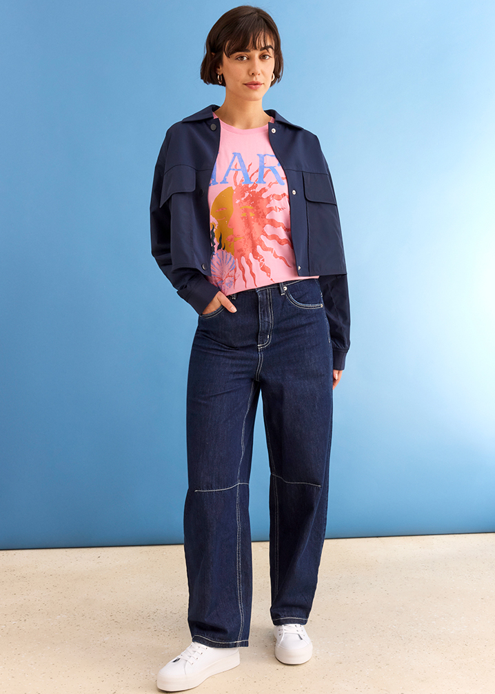 Dunkelblaue Jeansjacke über buntem Batik-Shirt, weite Jeans und weiße Sneaker bilden lässigen Look.