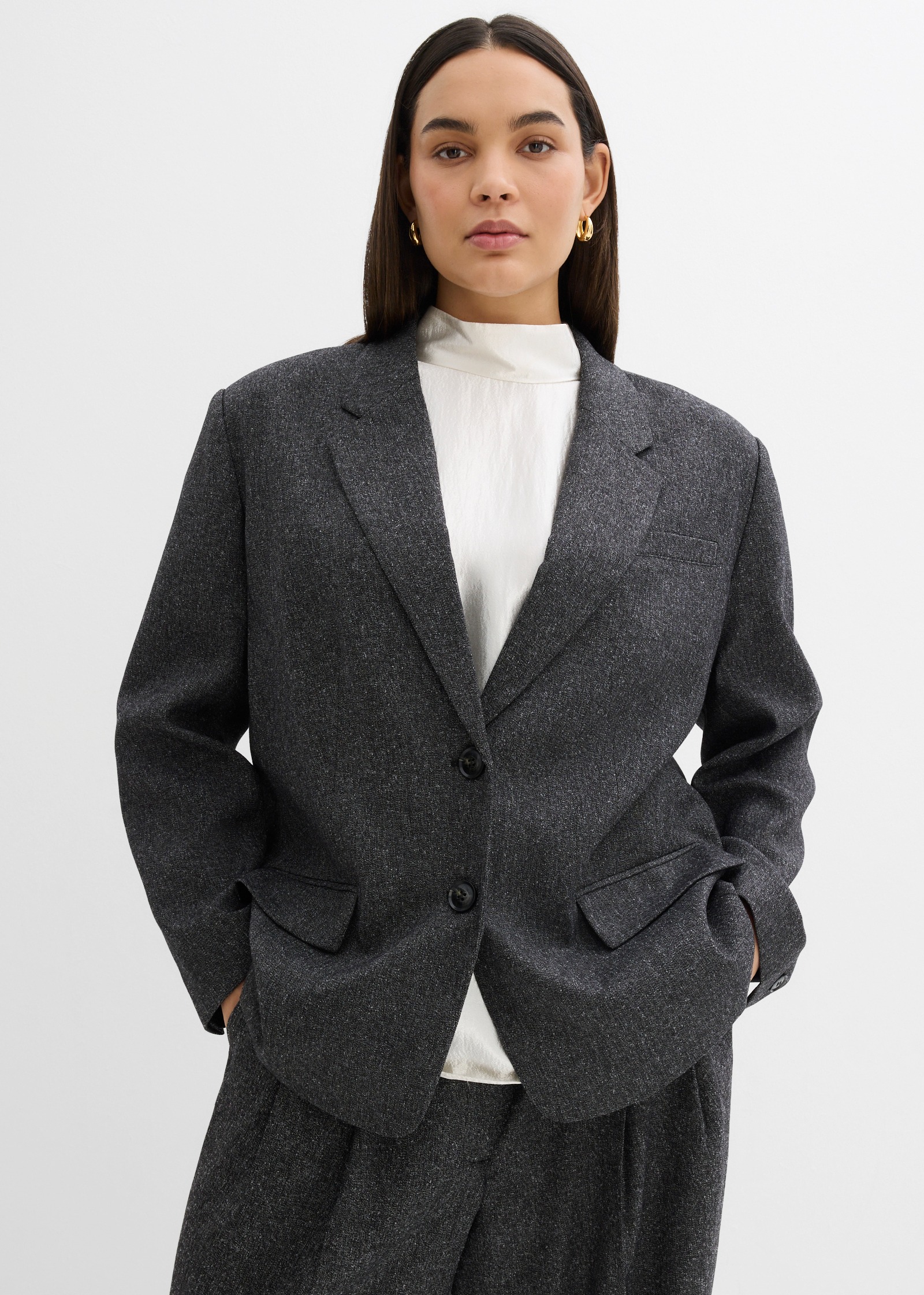 Grauen Struktur-Blazer, helle Bluse und graue Hose.