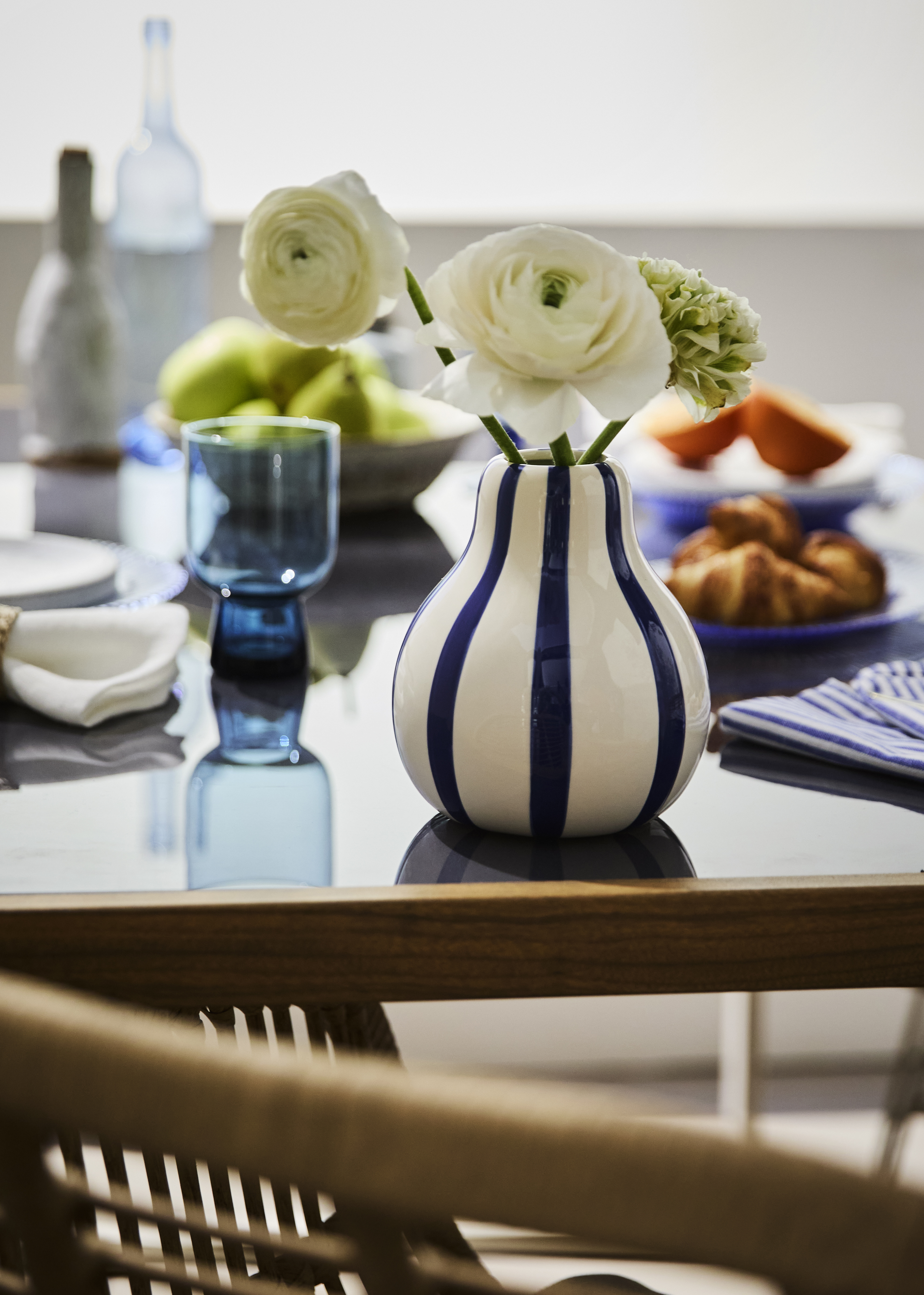Eine gestreifte Vase mit weißen Blumen ziert den Esstisch neben Gläsern und Tellern.