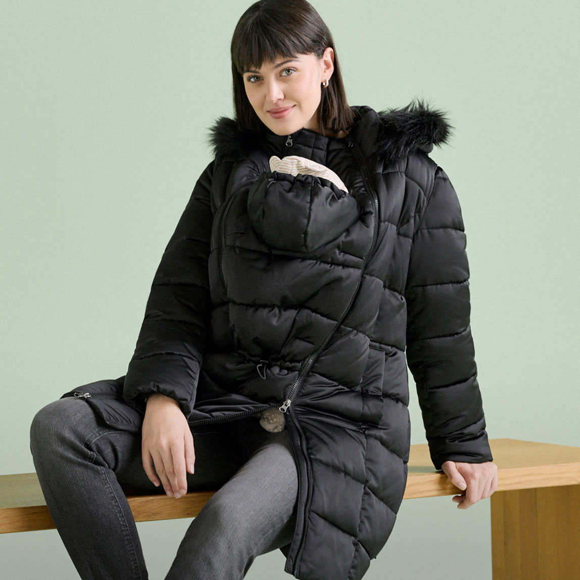 Schwarze Umstands-Pufferjacke mit Fellkapuze und praktischer Babytragefunktion.