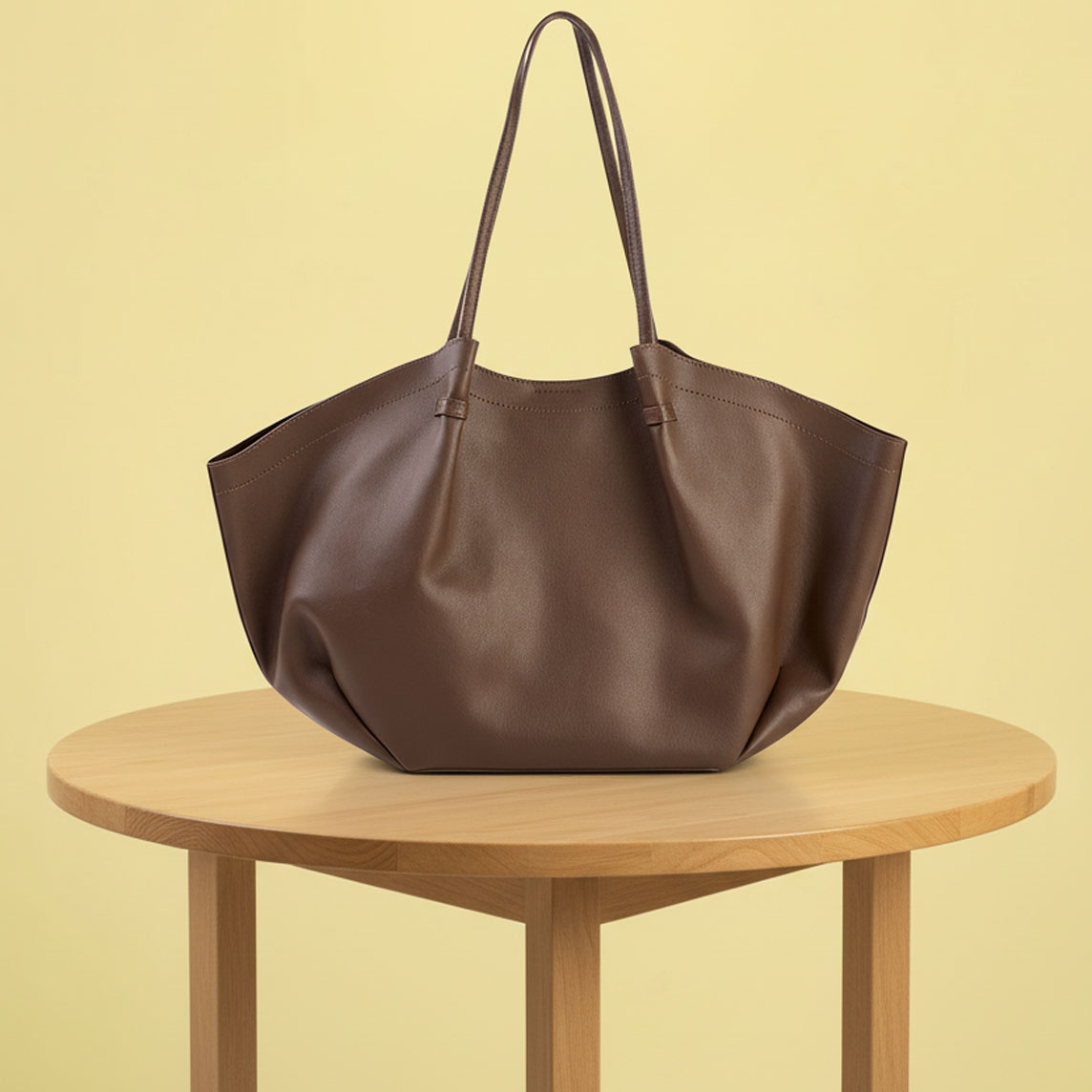 Eine elegante braune Ledertasche mit langen Henkeln steht auf einem runden Holztisch.