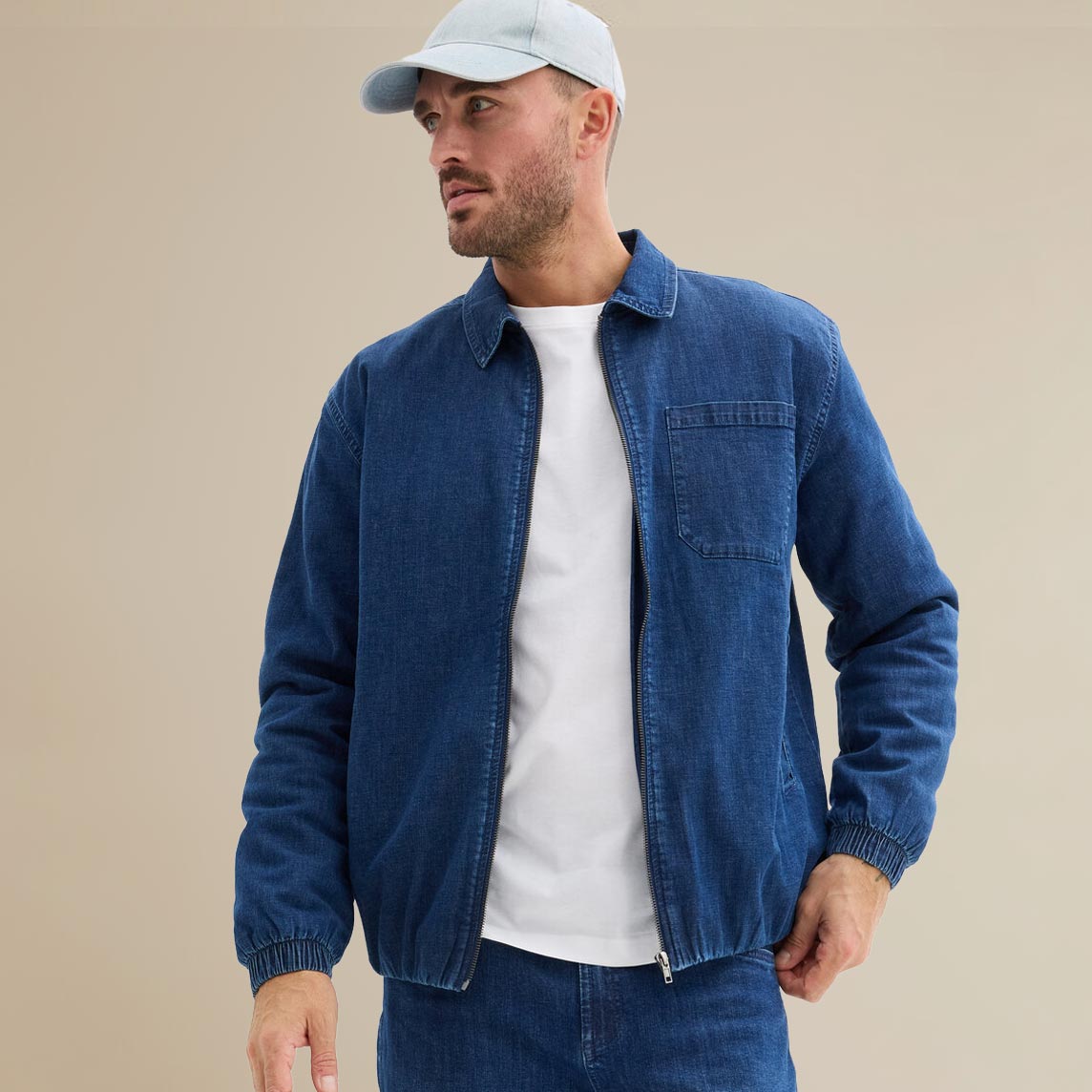 Blaue Jeansjacke über weißem Shirt, kombiniert mit weißer Cap.