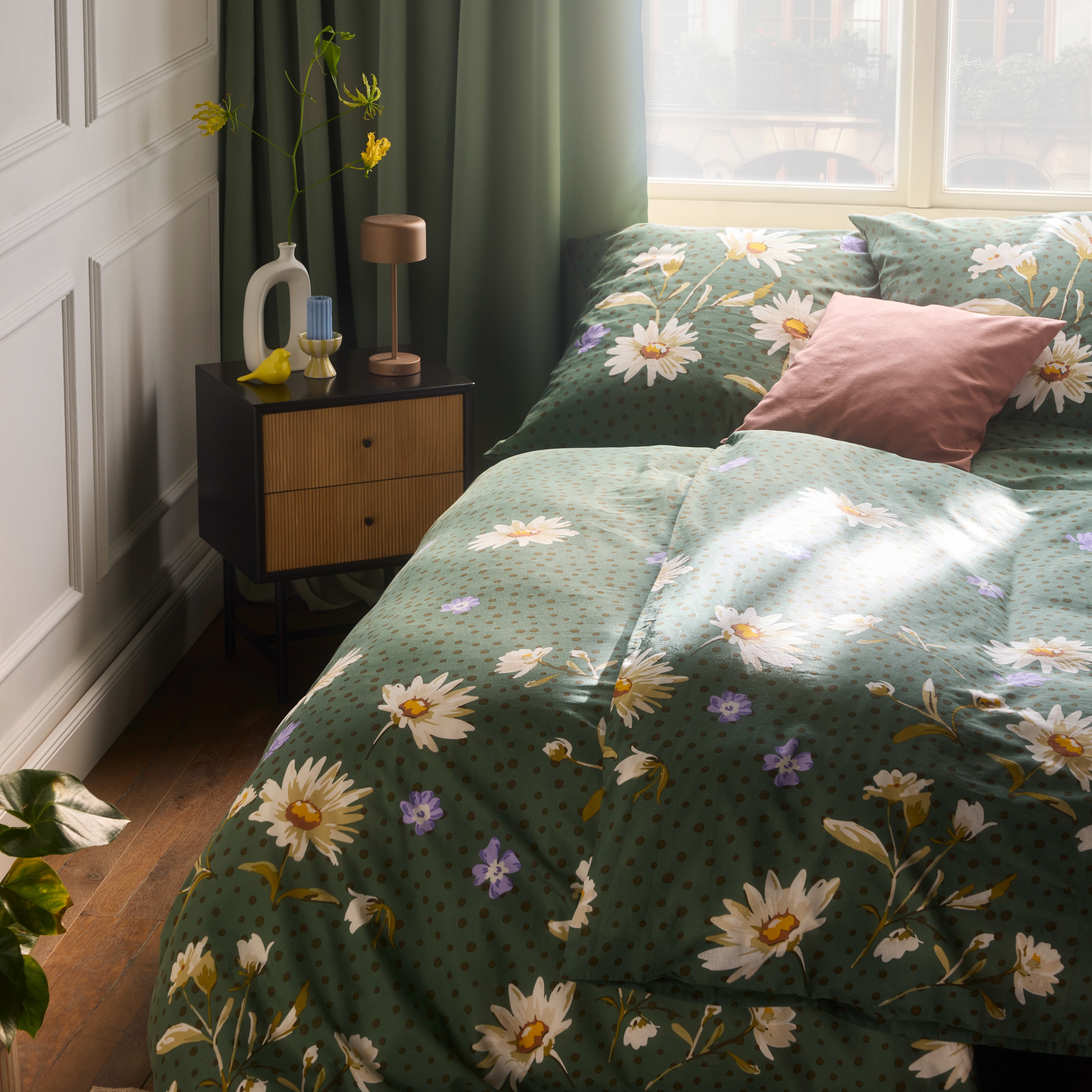 Blumige Bettwäsche in Grün schmückt das Bett, ergänzt durch passende Kissen.