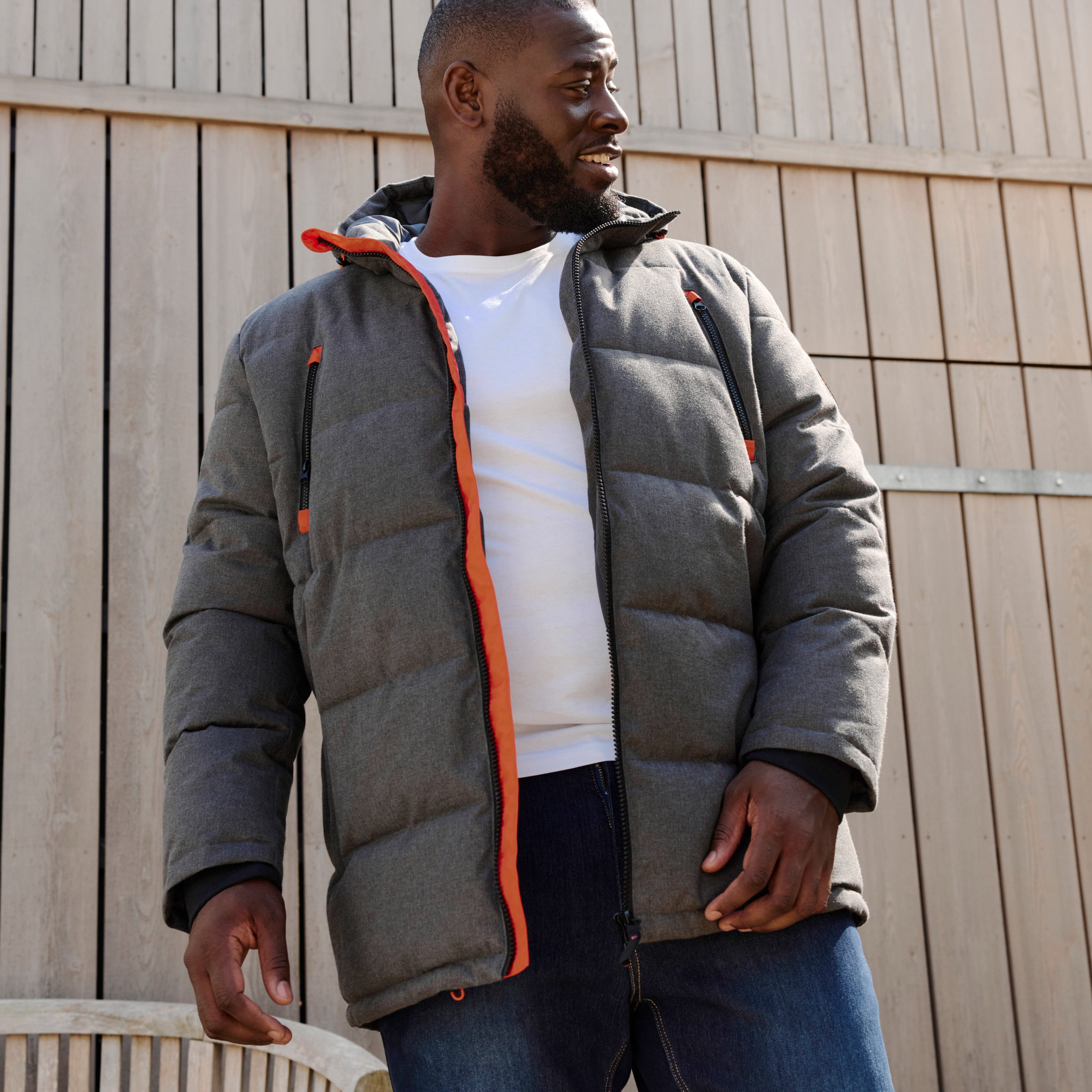 Graue Steppjacke mit orangen Akzenten, weißes T-Shirt und blaue Jeans.