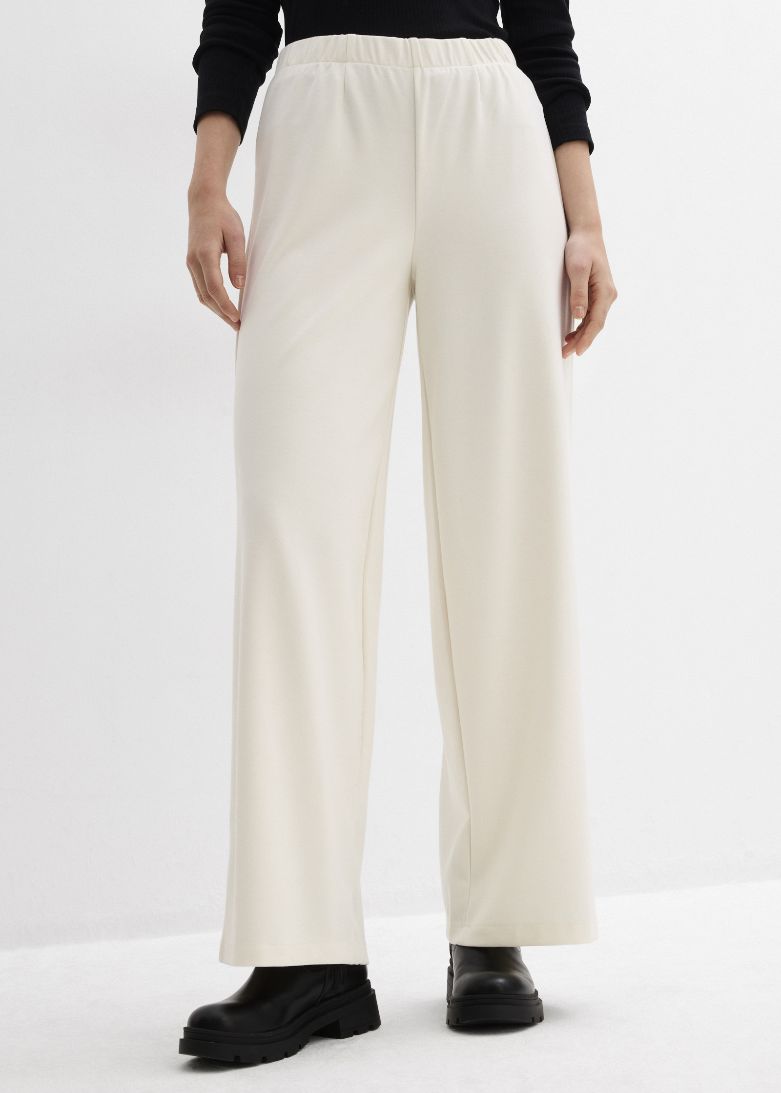 Cremefarbene weite Hose mit schwarzem Oberteil und klobigen schwarzen Schuhen.