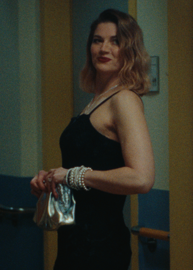 Frau trägt ein schwarzes Kleid, Perlenkette, Perlenarmbänder und eine silberne Clutch.