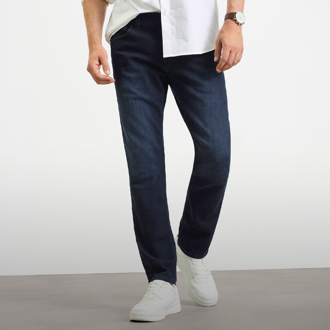 Dunkelblaue Slim-Fit Jeans, weißes Hemd und weiße Sneaker.