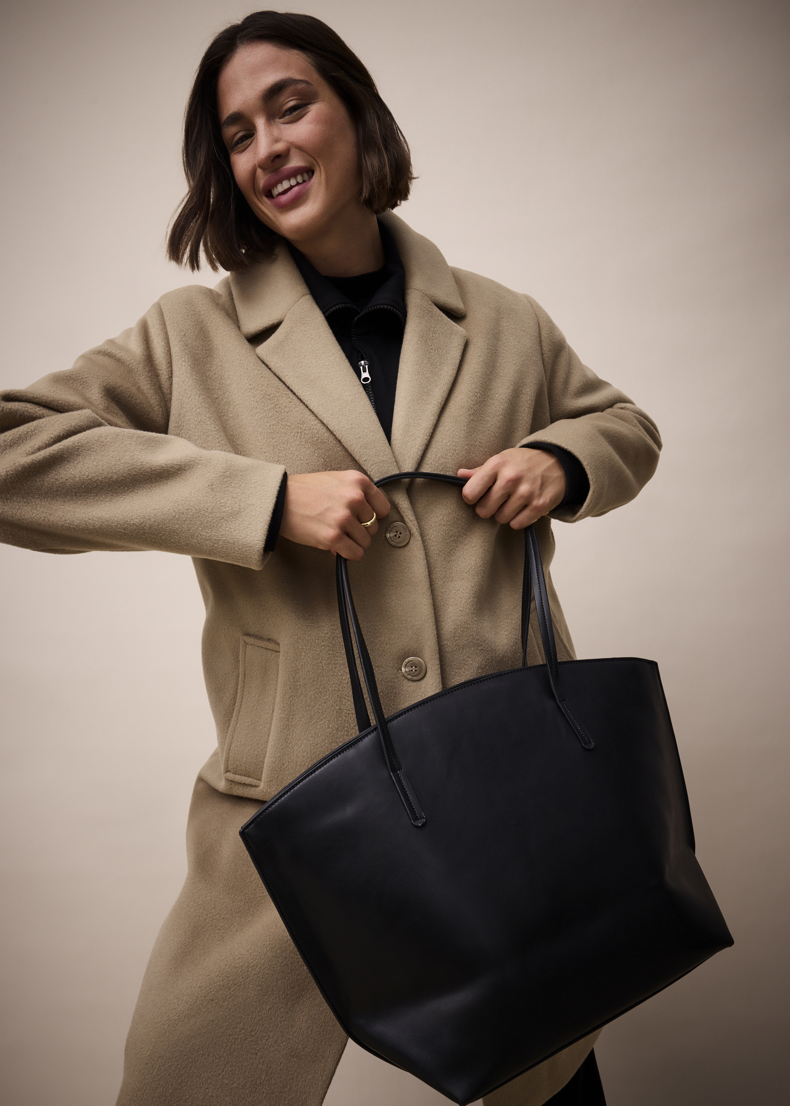 Eleganter beigefarbener Mantel mit großen Knöpfen, kombiniert mit schwarzer Handtasche und dunklem Oberteil.