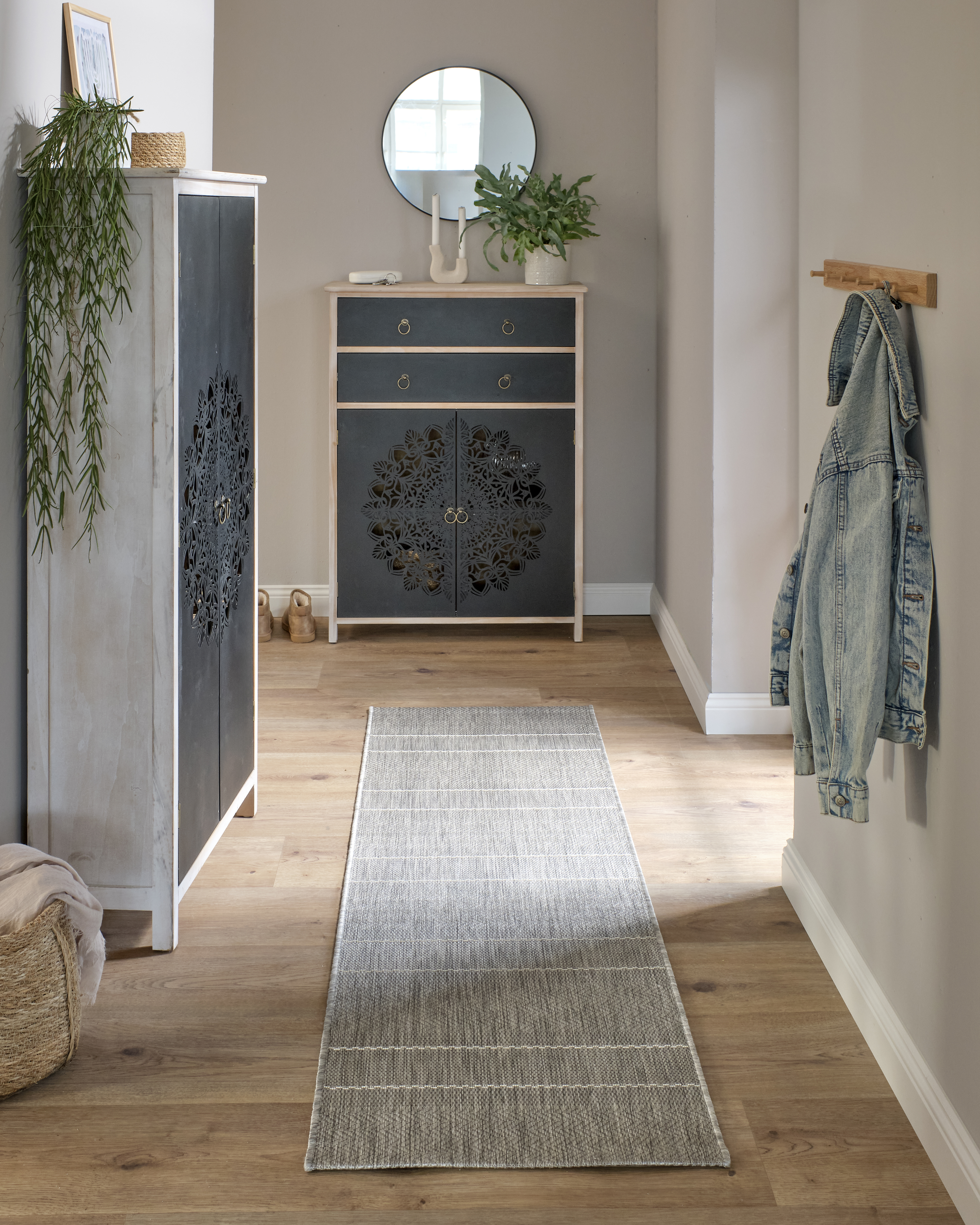 Modernes Wohnzimmer mit schwarzer Kommode, Holzlamellen, Tischlampe und rundem Hocker auf Teppich.