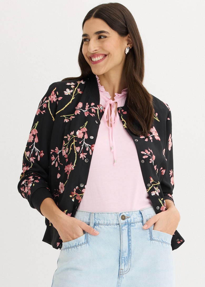 Schwarze Bomberjacke mit Blütenmuster über pinkem Top, kombiniert mit heller Jeans.