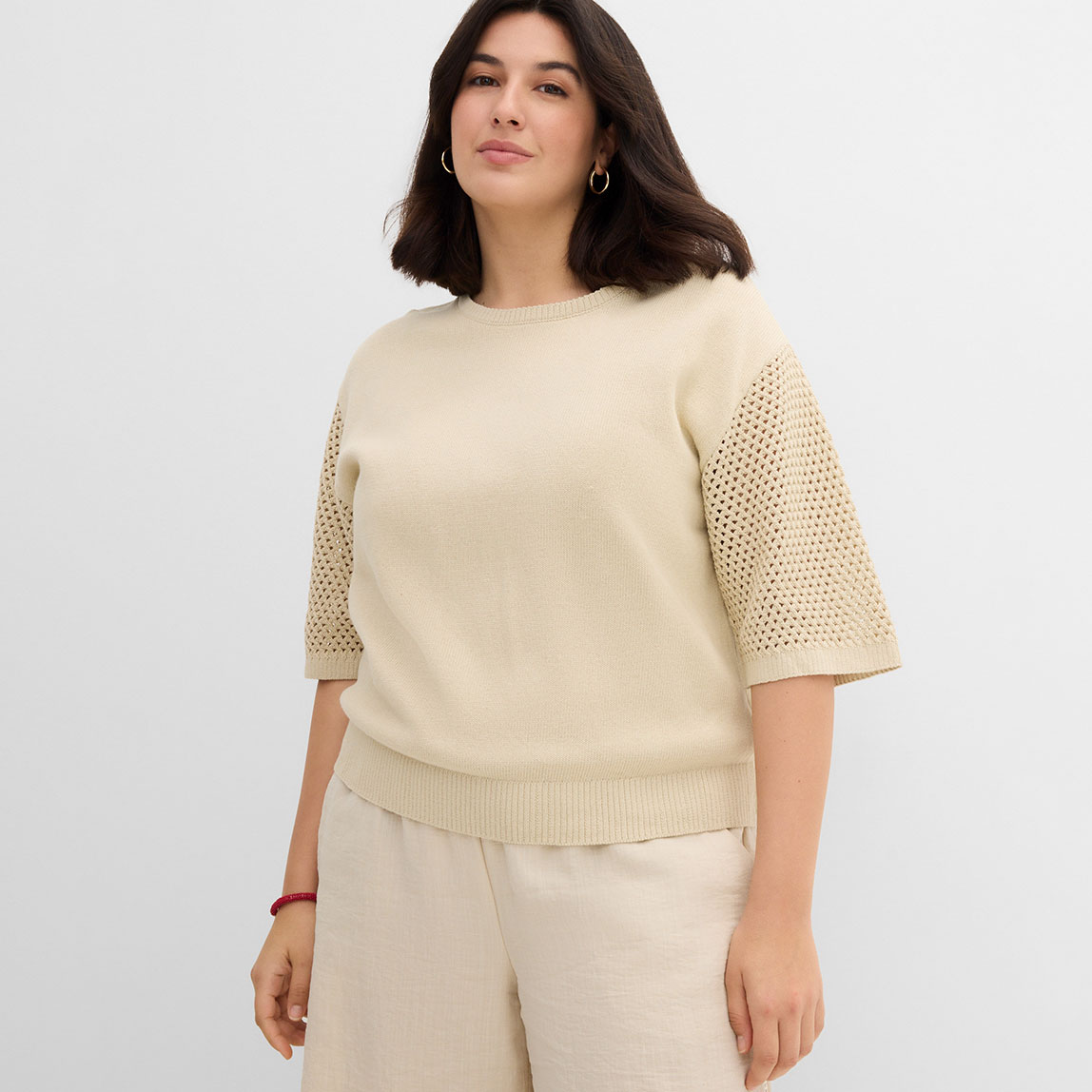 Beiger Pullover mit durchbrochenen Ärmeln und passender heller Hose im modernen Look.
