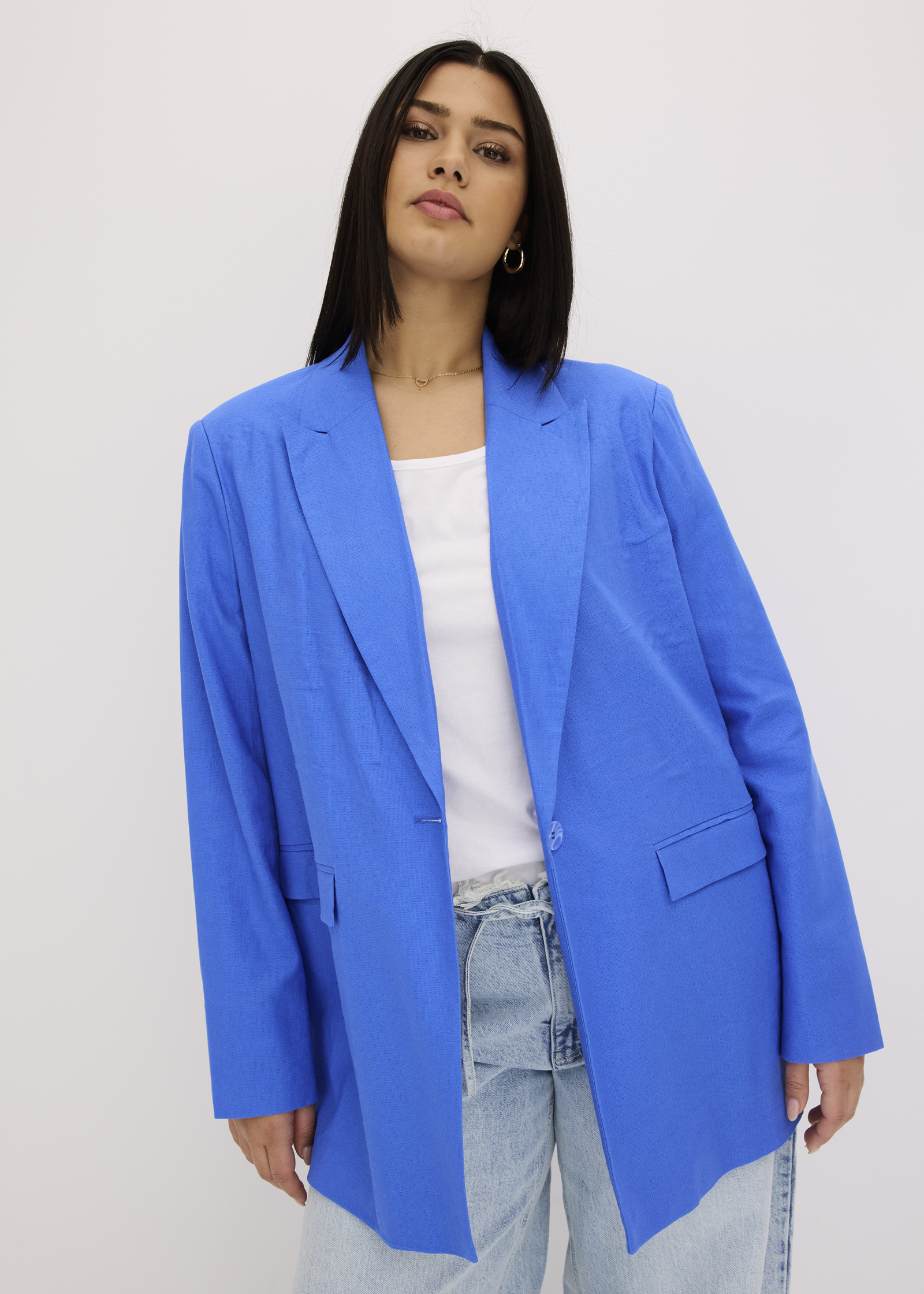 Sie trägt einen blauen Blazer, ein weißes Top und weite Jeans.