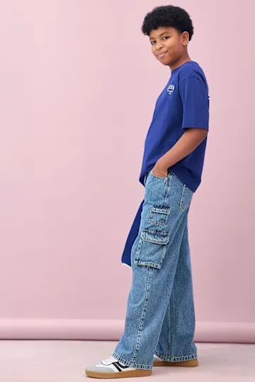 Der Junge trägt ein blaues T-Shirt und weite Cargo-Jeans.