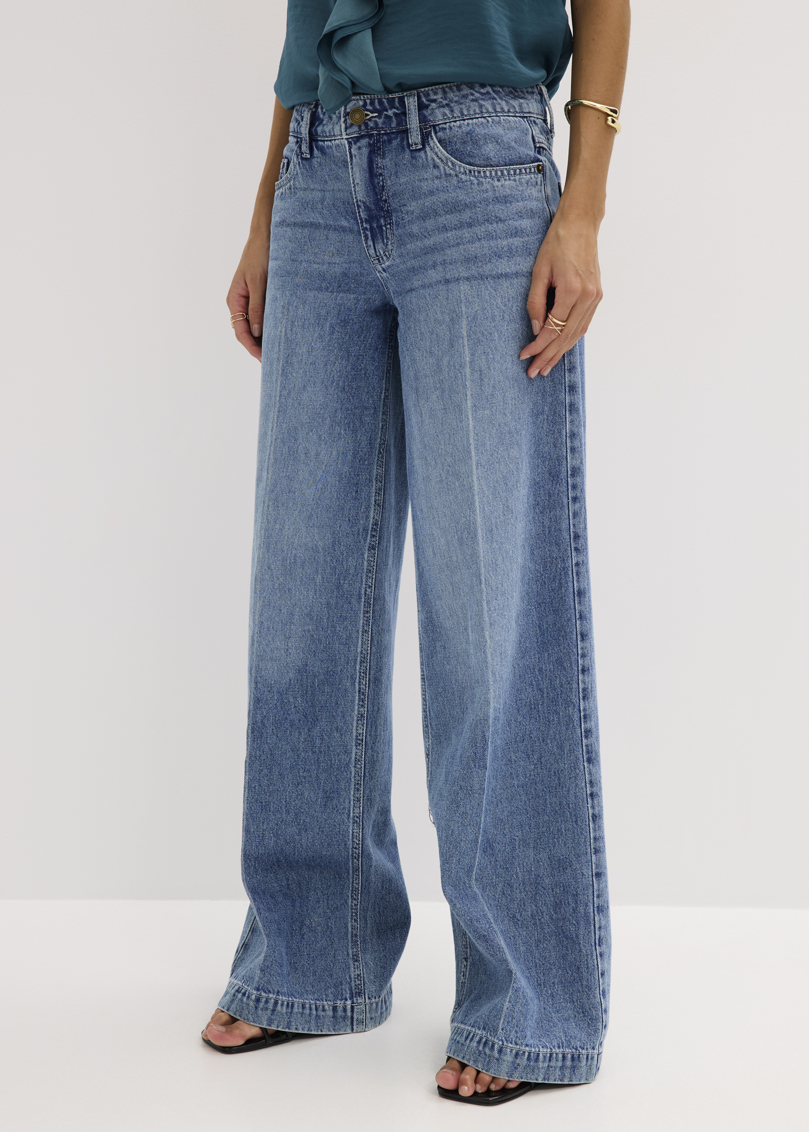 Weite Jeans in heller Waschung, kombiniert mit eleganter türkiser Bluse und Sandalen.