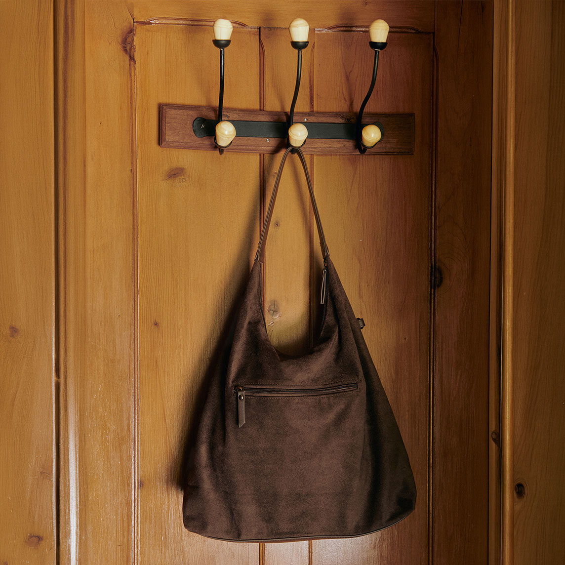 Eine stilvolle braune Tasche hängt an der hölzernen Wandgarderobe mit Messinghaken.