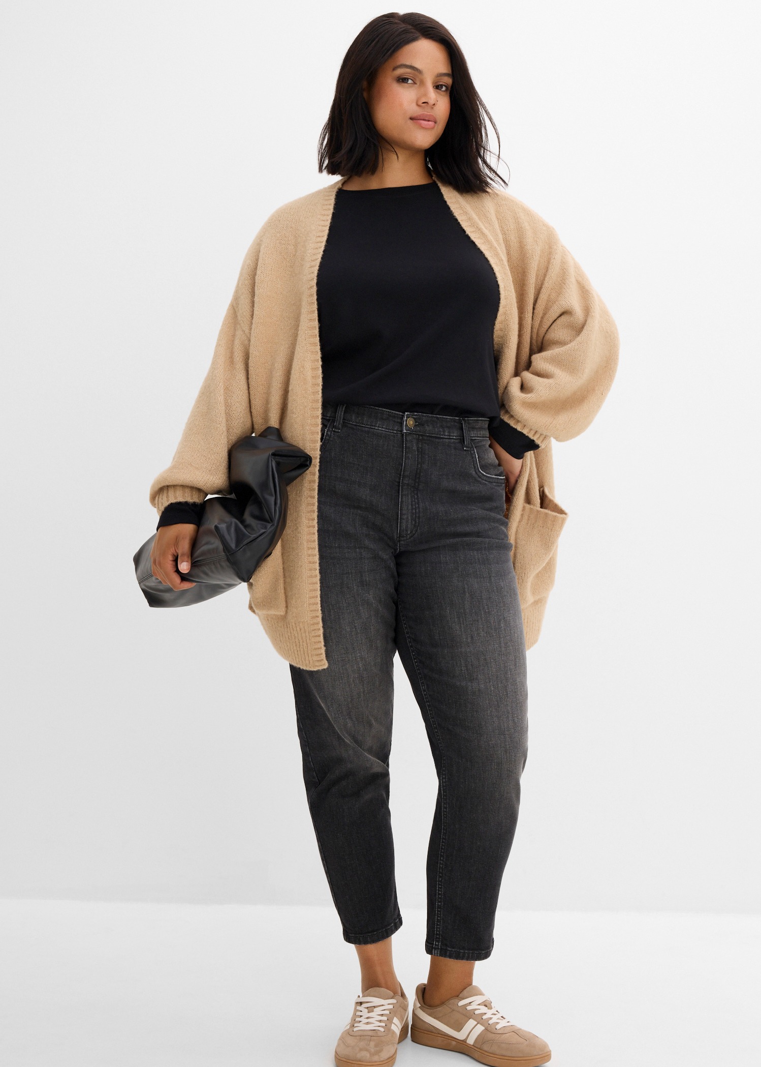Beiger Strickcardigan über schwarzem Oberteil, dazu graue Jeans und beige Sneaker.