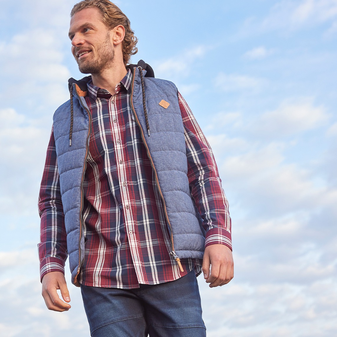 Kariertes Hemd, blaue Jeans und graue Weste. 