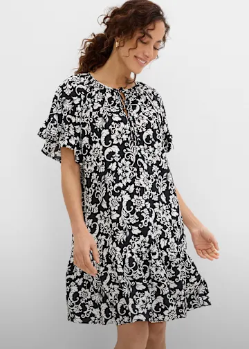 Locker sitzendes Kleid in Schwarz-Weiß mit floralem Muster und eleganten Rüschenärmeln.