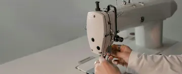 Hände bedienen eine Nähmaschine.