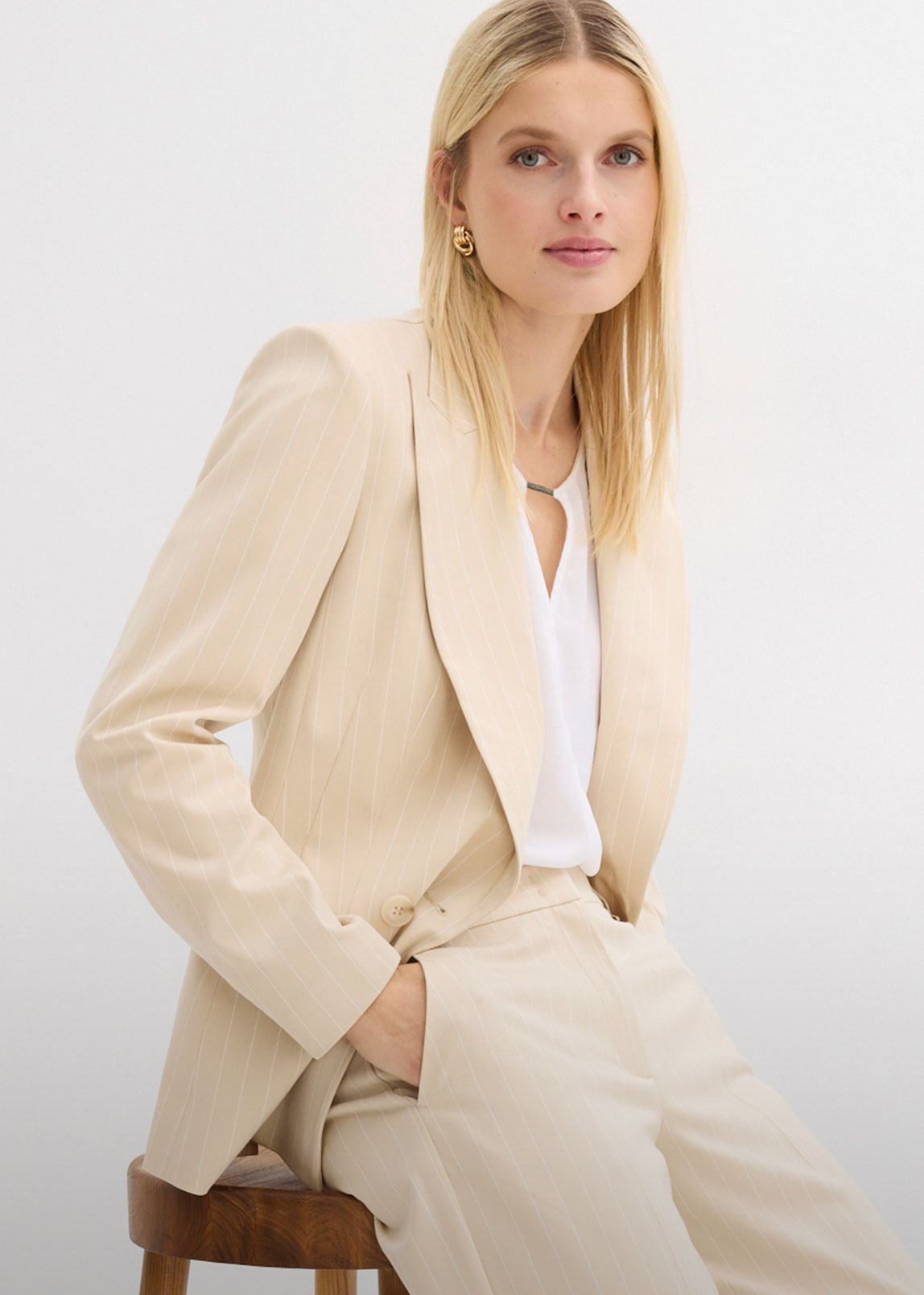 Eleganter beiger Nadelstreifen-Blazer kombiniert mit weißer Bluse und passender Hose.