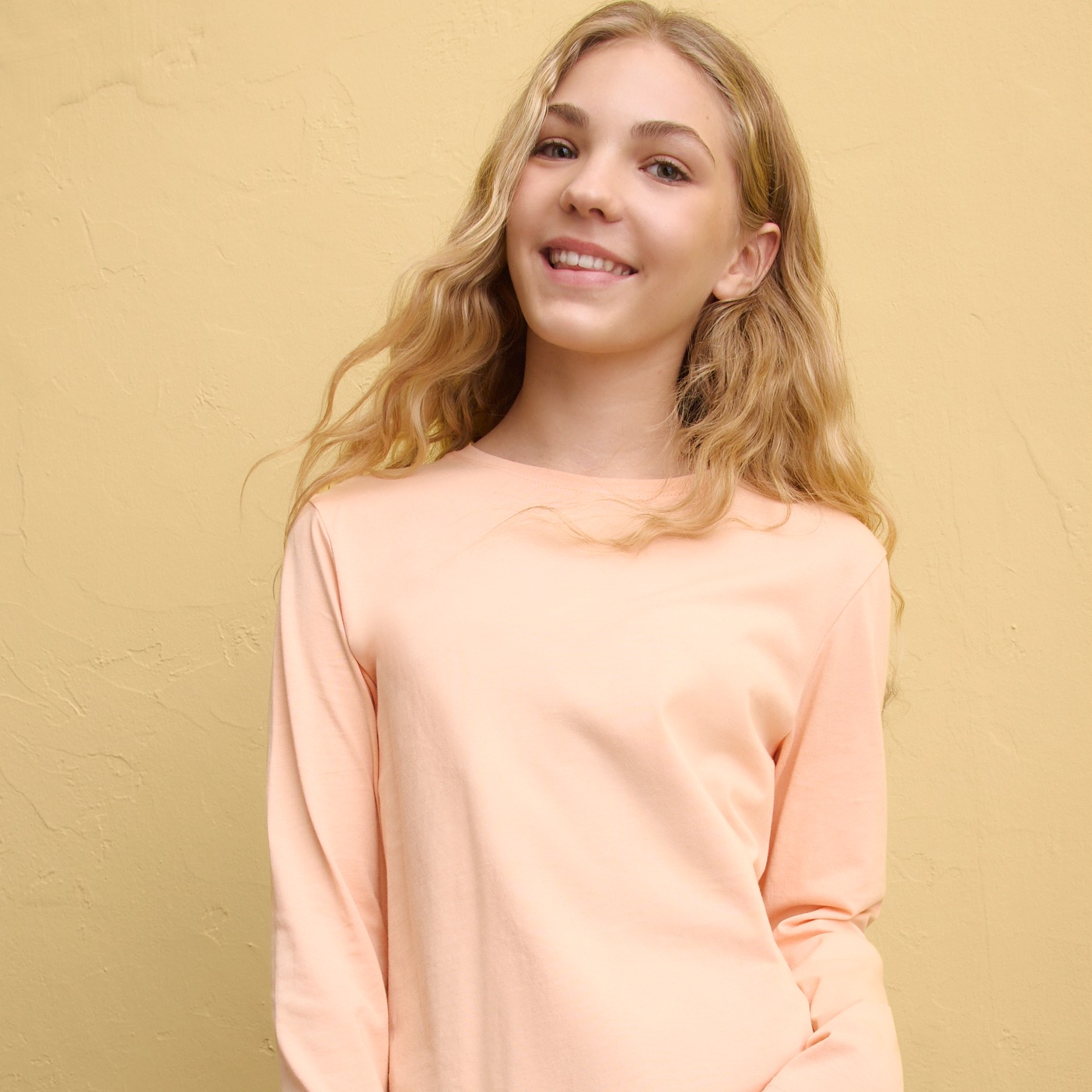 Zartes Pfirsichfarben trifft auf dunkles Denim: Lässiger Look mit Pullover und Jeans.