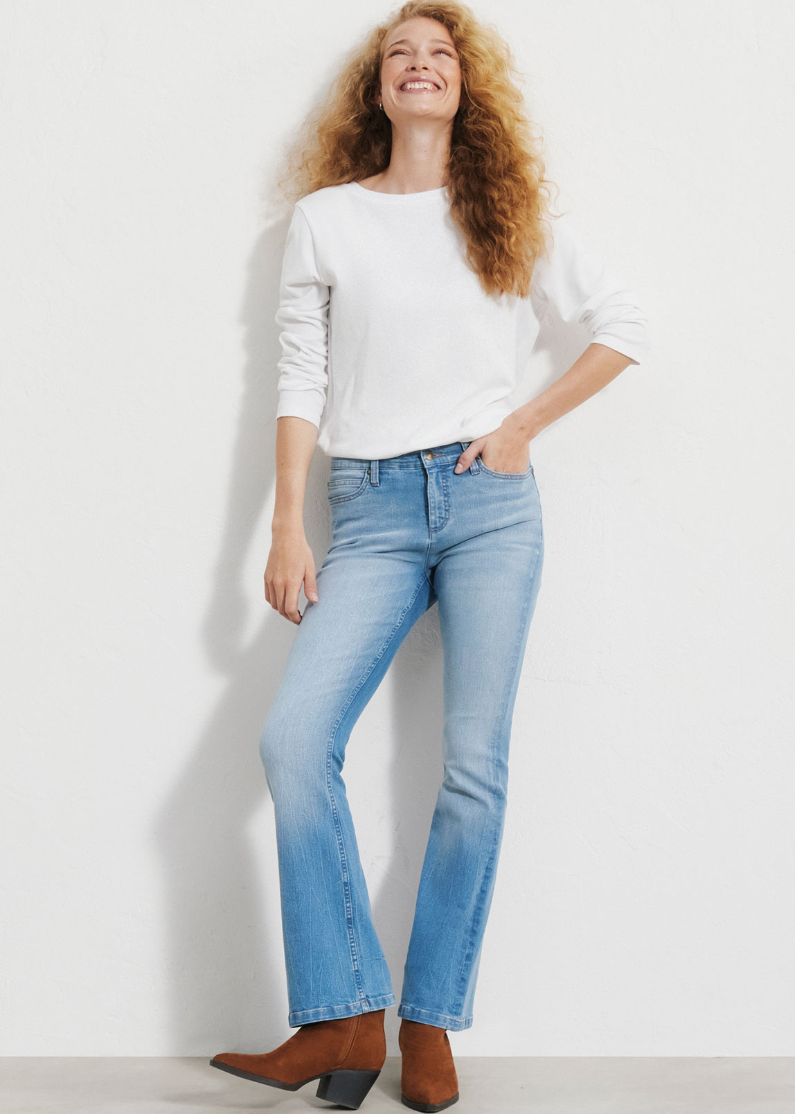 Weißes Langarmshirt, helle Bootcut-Jeans und braunen Stiefeletten.