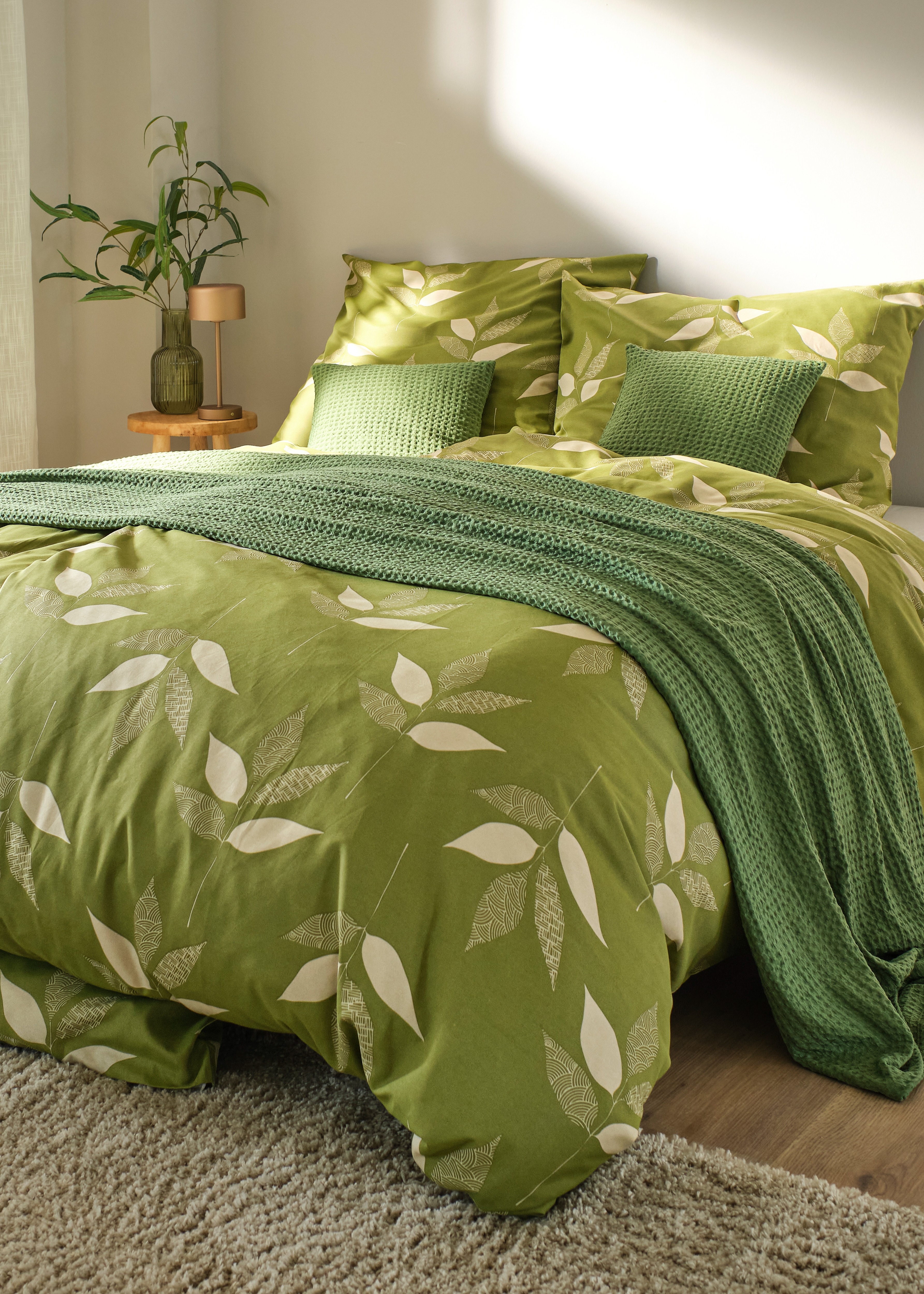 Auf dem Bett liegt eine grüne Tagesdecke.