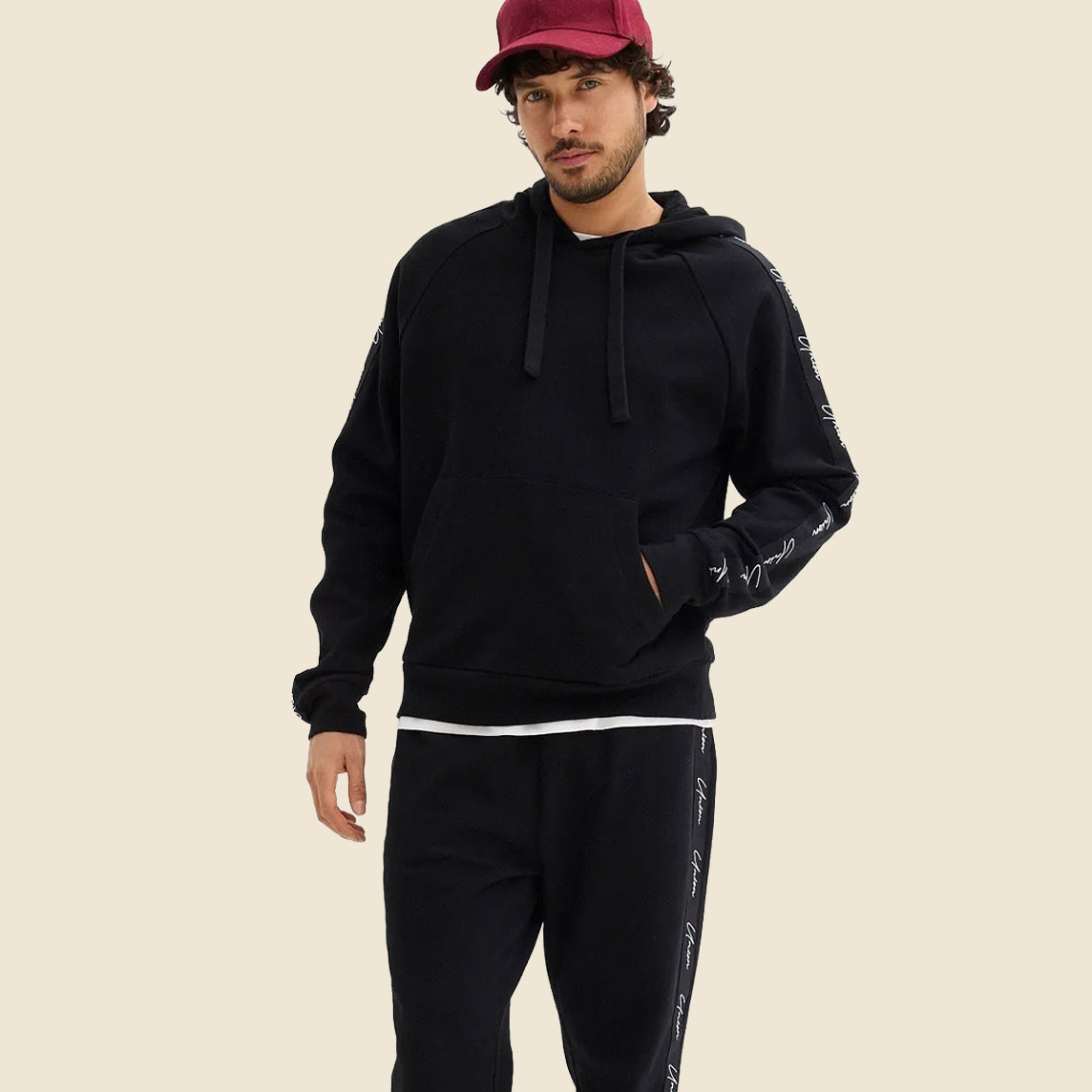 Lässiger schwarzer Hoodie und Jogginghose mit Schriftzügen, dazu rote Kappe.