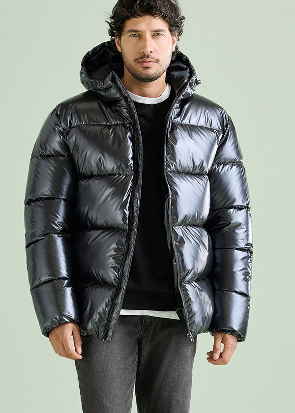 Moderne schwarze Glanz-Steppjacke mit Kapuze, schwarzer Pulli, dazu graue Jeans.