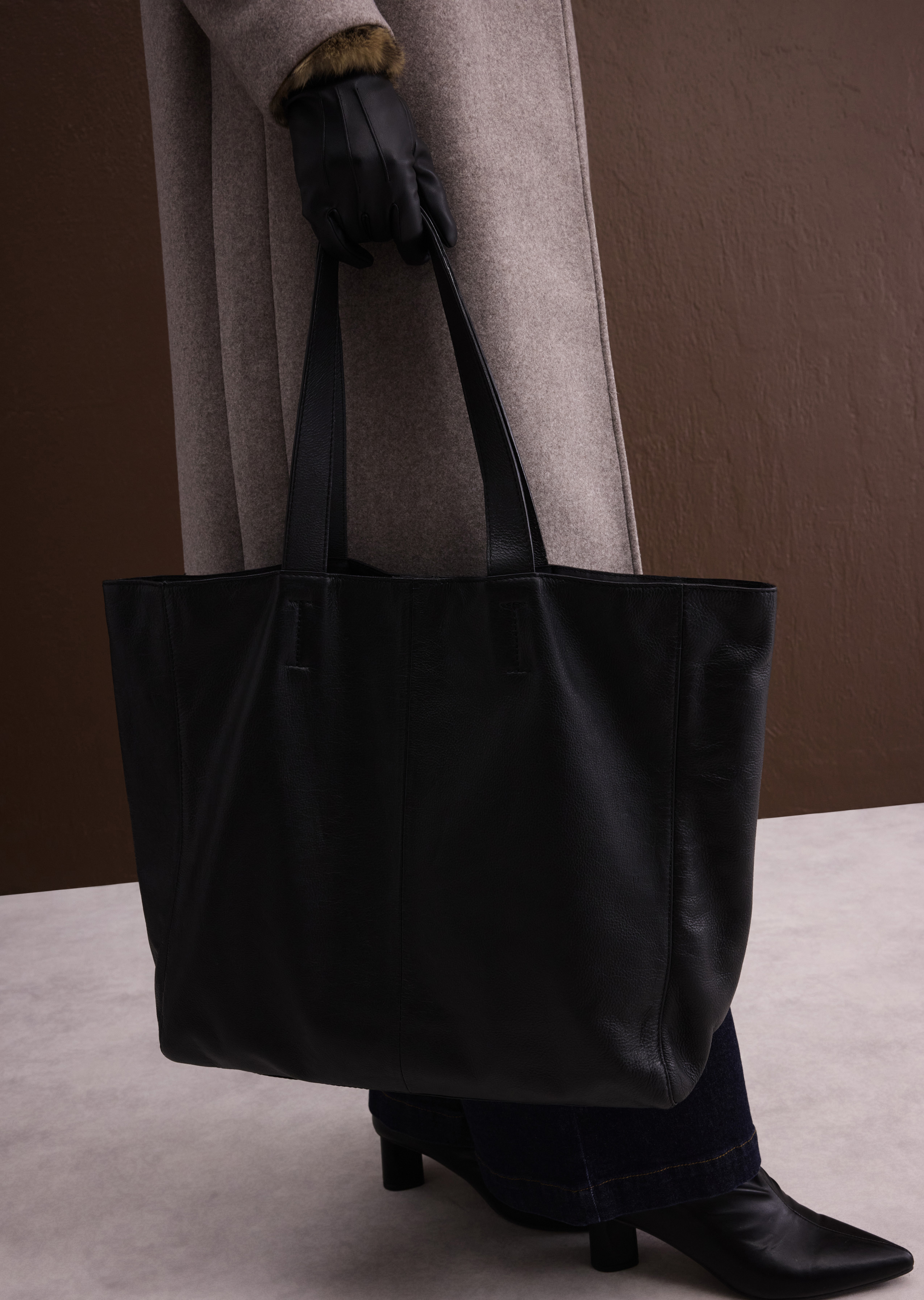 Warmer Mantel, elegante Handschuhe, Jeans und Stiefel, dazu eine schicke Ledertasche.