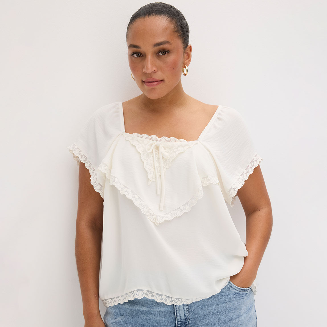 Eine weißes Blusentop mit Spitzendetails und Rüschen.
