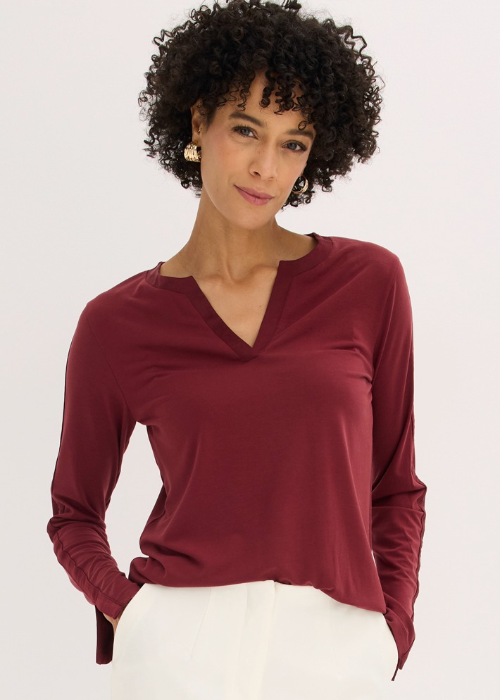 Bordeauxrotes Langarmshirt mit V-Ausschnitt und weiße Hose ergeben ein stilvolles Outfit.