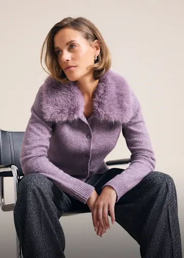 Fliederfarbene Strickjacke mit Fellkragen und glitzernde Hose, ein stilvoller Look.