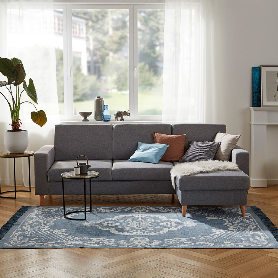 Graues Ecksofa mit braunen und blauen Kissen in hellem, modernem Wohnzimmer.
