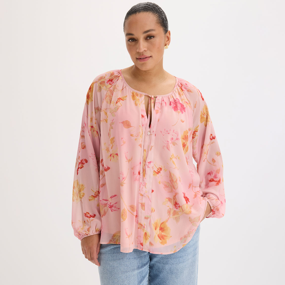 Fließende rosa Bluse mit buntem Blumenmuster und dekorativen Bändern am Ausschnitt.