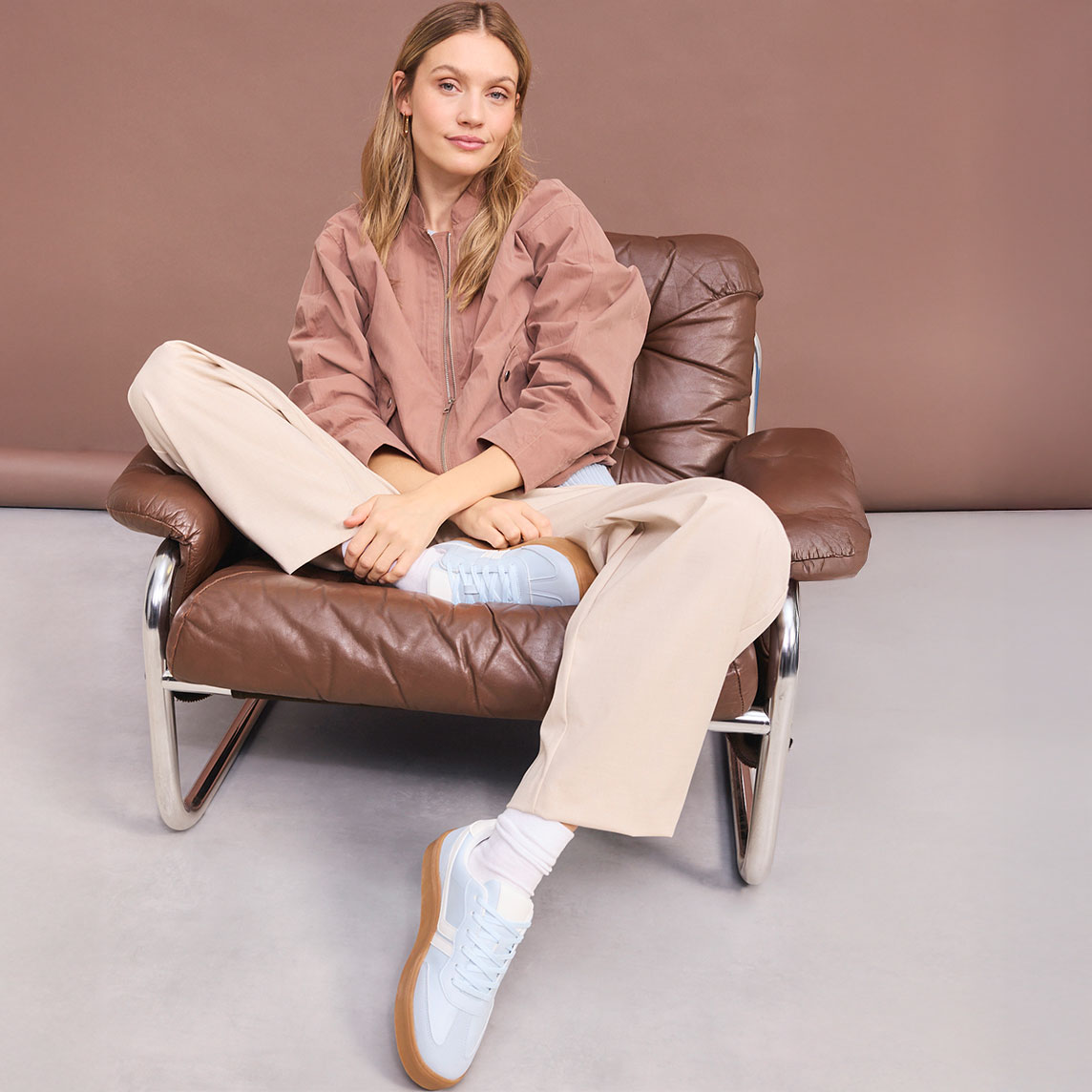 Braune Jacke kombiniert zur beigen Hose und hellblauen Sneaker.