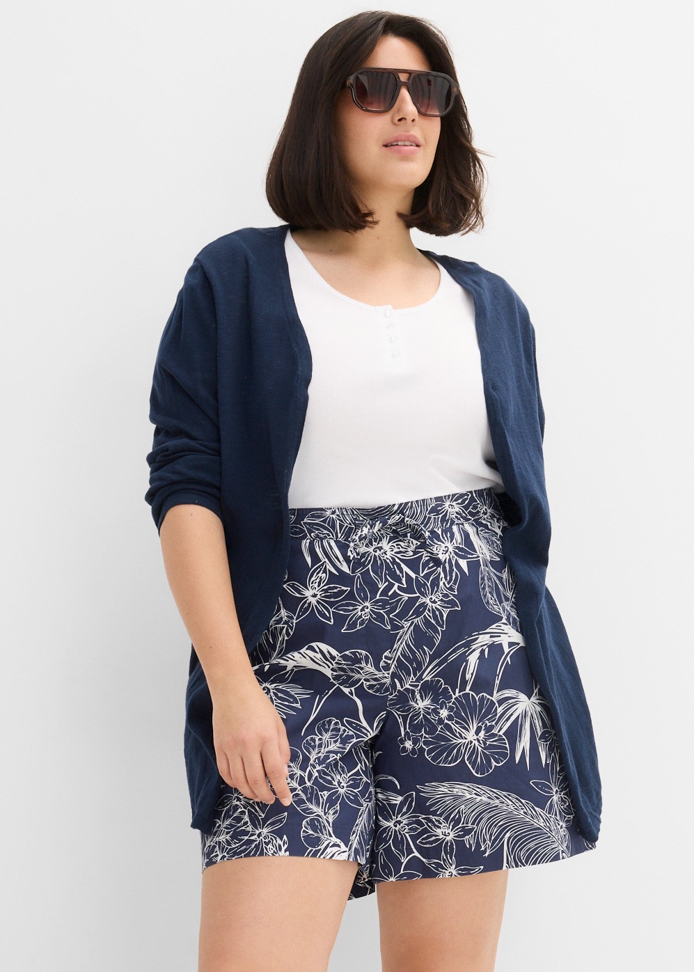 Marineblauer Cardigan, weißes Top und gemusterte Shorts.