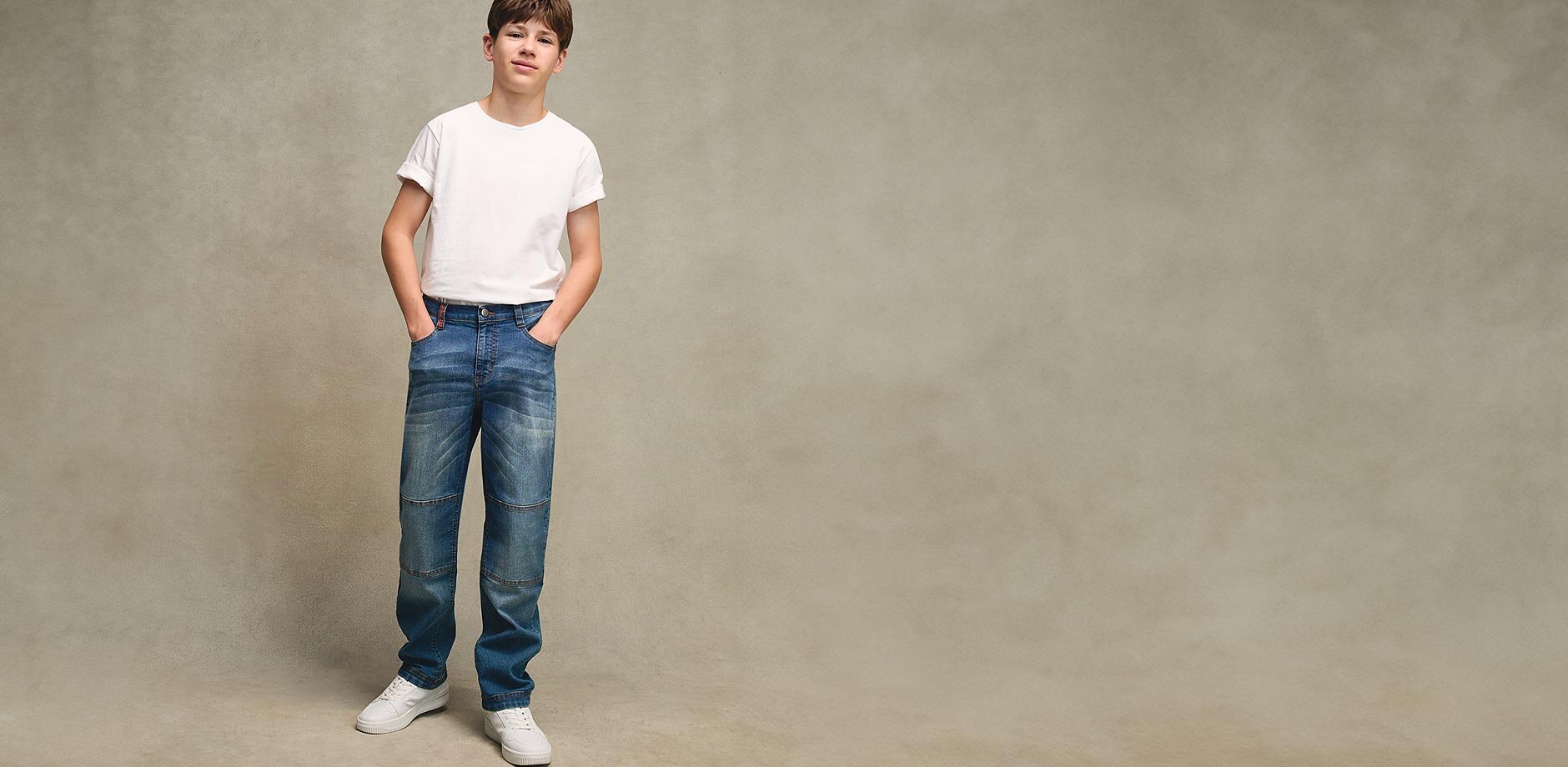 Legere Alltagskleidung: Weißes T-Shirt mit Muster, blaue Jeans und helle Sneakers.