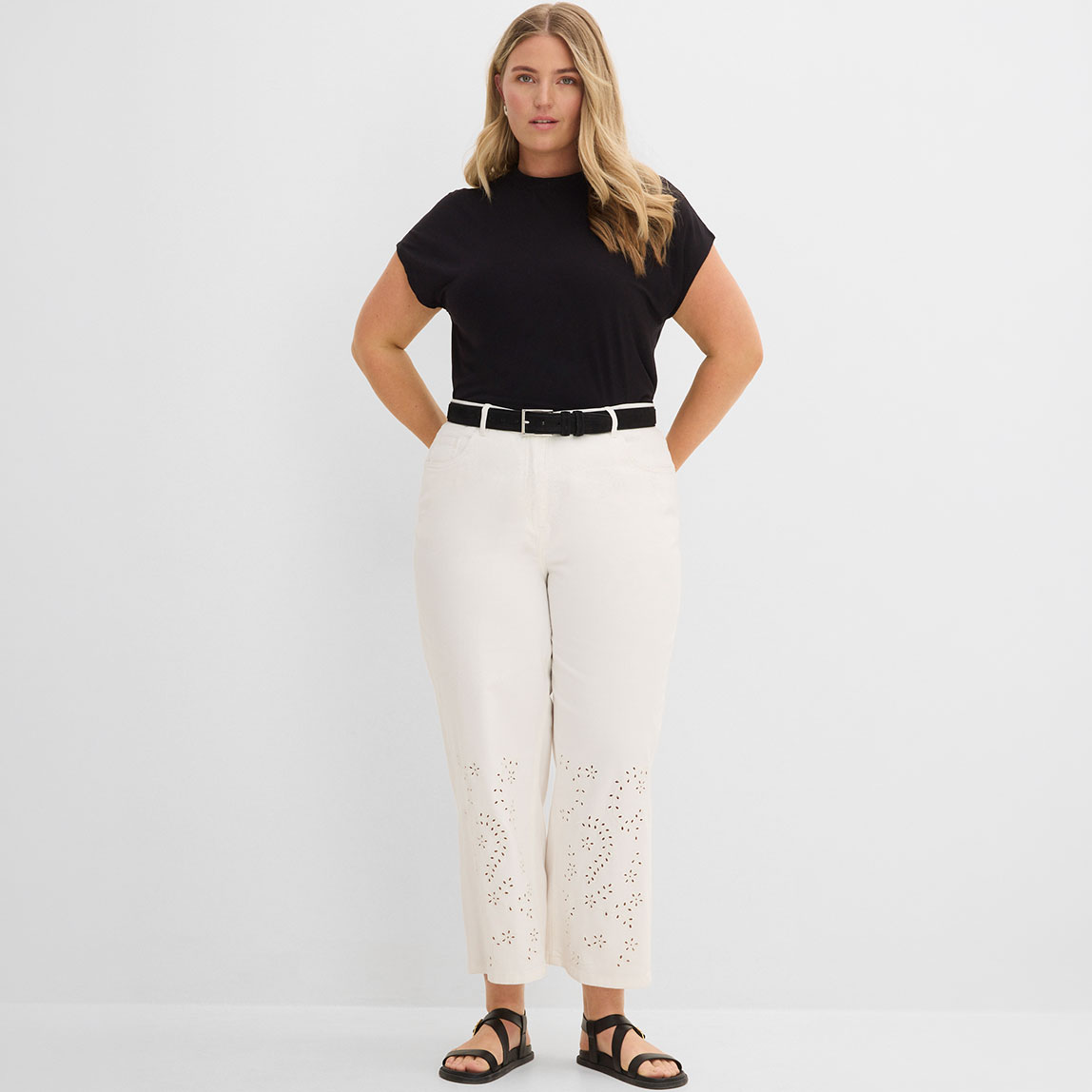 Schwarzes T-Shirt, cremefarbene Lochstickereihose und schwarze Sandalen.
