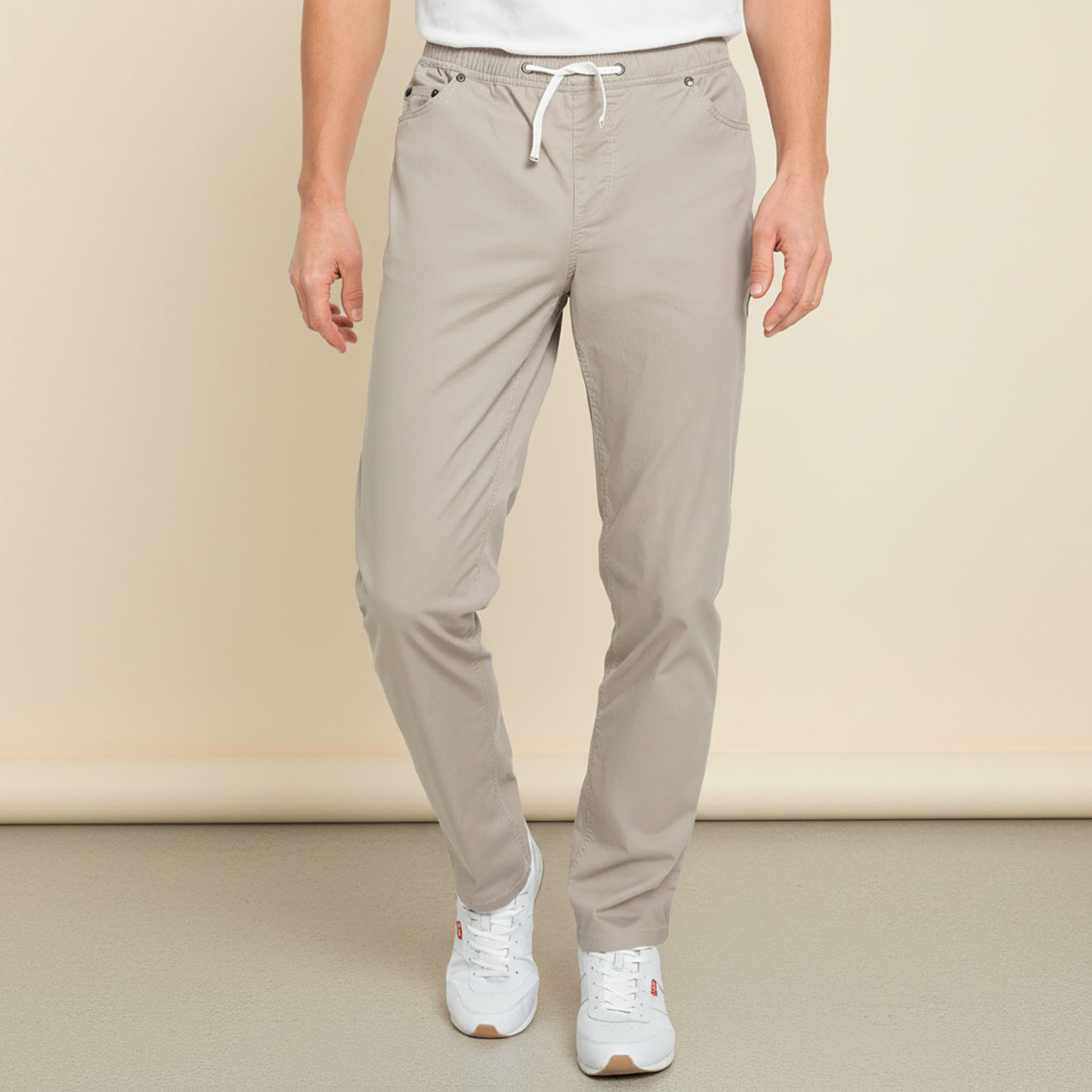 Bequeme beige Hose mit Kordelzug, weißem T-Shirt und sportlichen Sneakern.