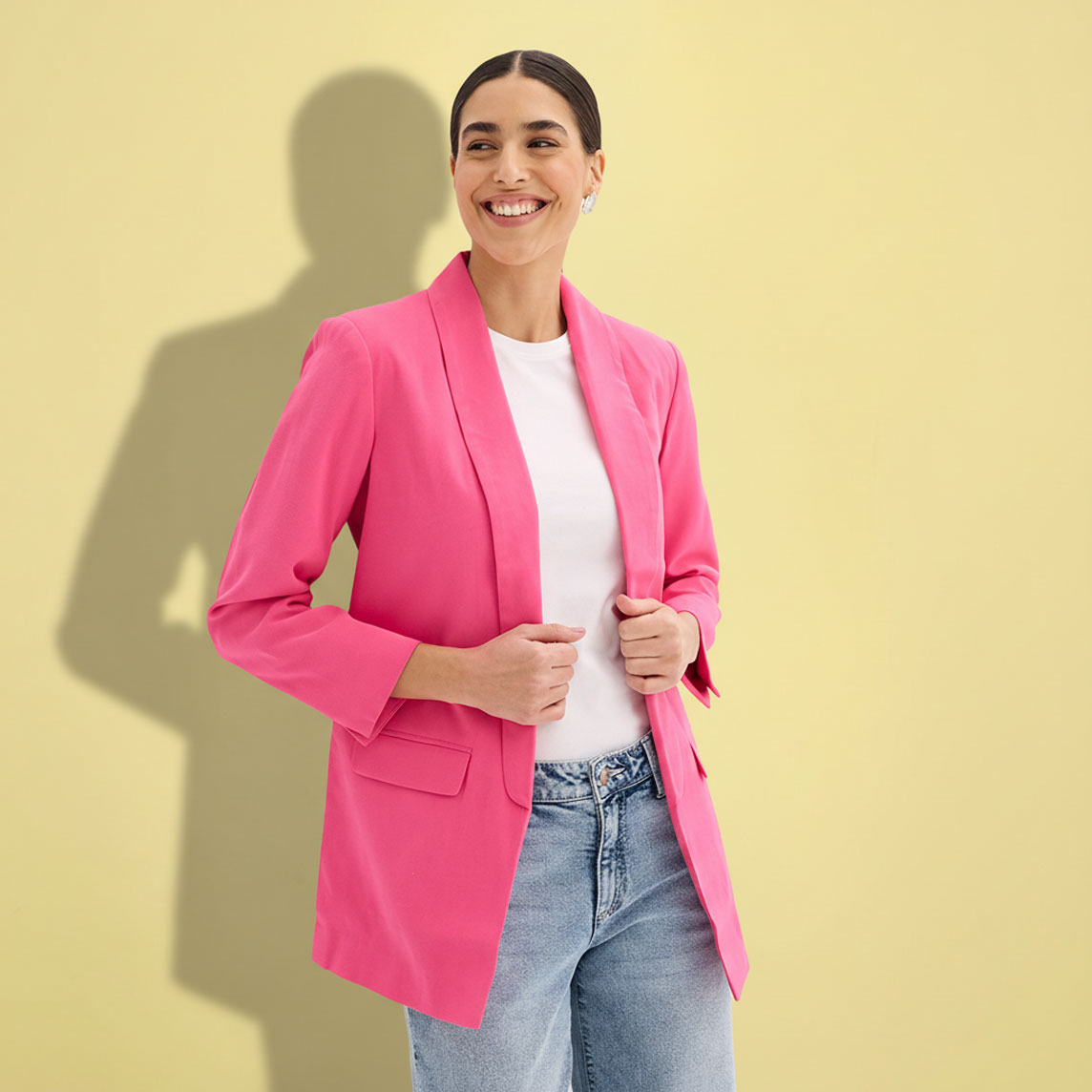 Eine Frau trägt einen pinken Blazer über einem weißen Top und blauen Jeans.