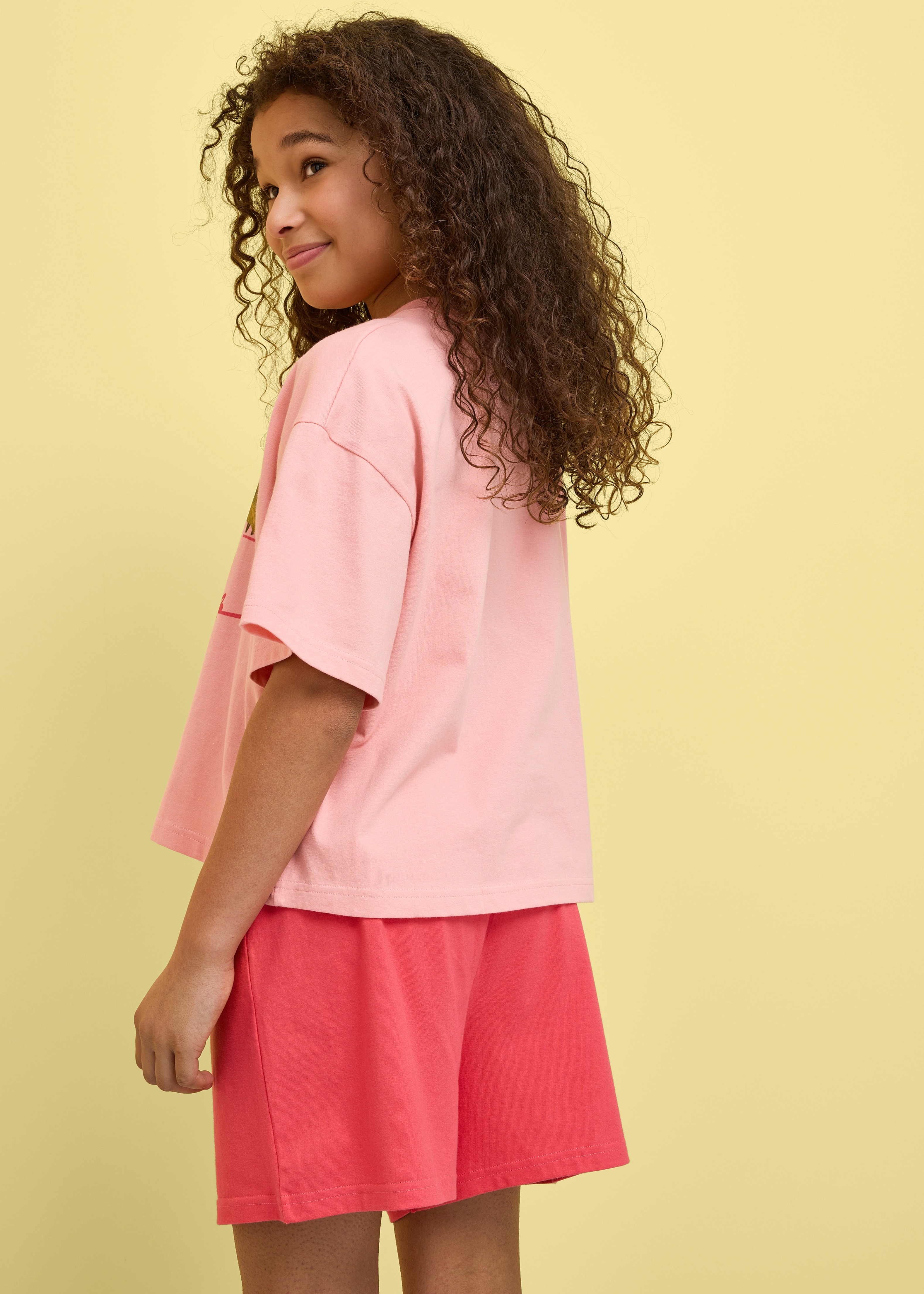 Das Mädchen trägt ein lockeres rosa T-Shirt und bequeme rote Shorts.