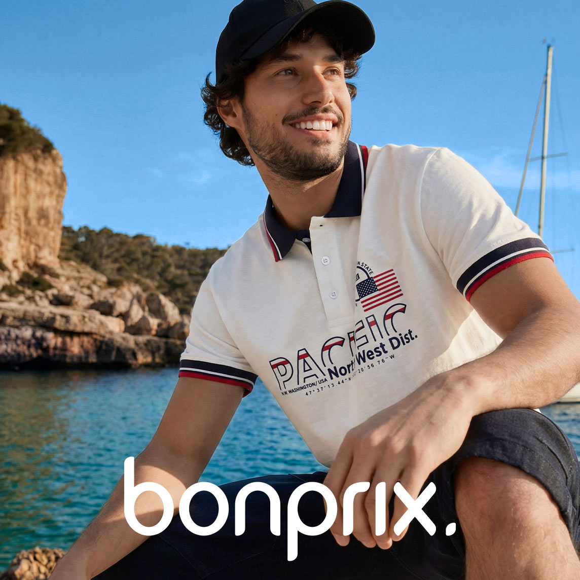 Weißes Poloshirt Schriftzug, dazu schwarze Baseballkappe am Meer.