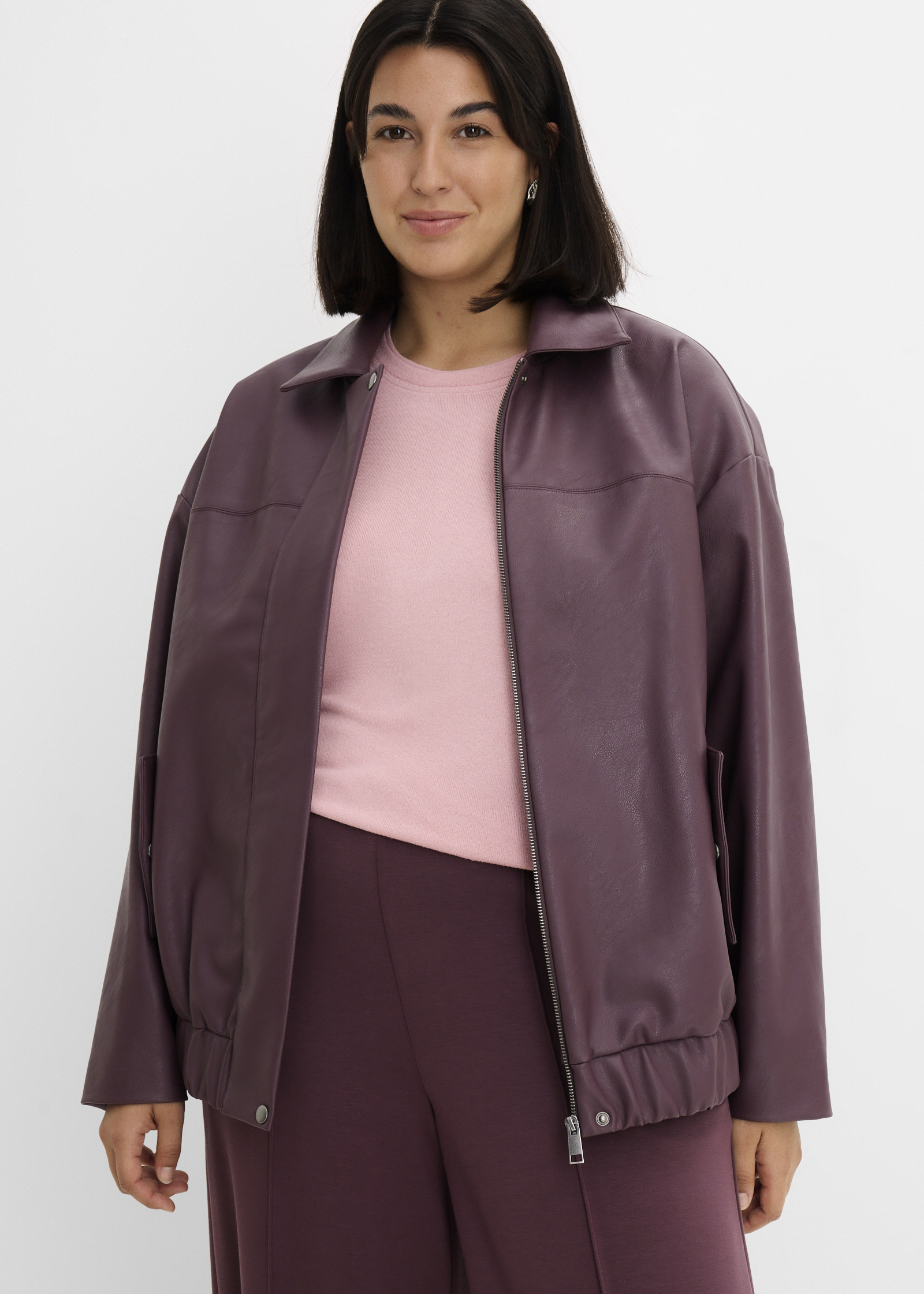 Lila Kunstlederjacke über rosa Oberteil, kombiniert mit passender Hose.