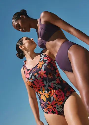 Zwei Frauen in Bademode blicken sich an, unter blauem Sommerhimmel.